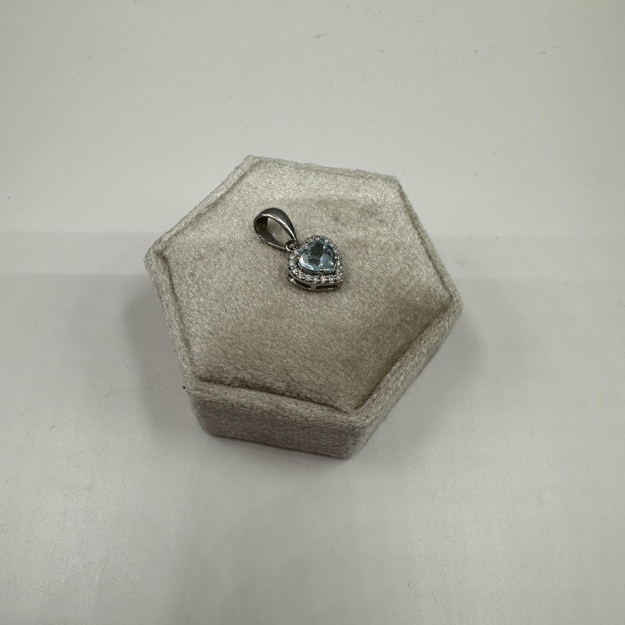 Questa elegante collana con cuore di topazio e diamanti in oro bianco 14 carati presenta un topazio blu con taglio a cuore di 5x5 mm, impreziosito da 0,10 carati di diamanti tondi naturali GH SI. Con un peso di soli 1.06 grammi, è leggero e comodo
