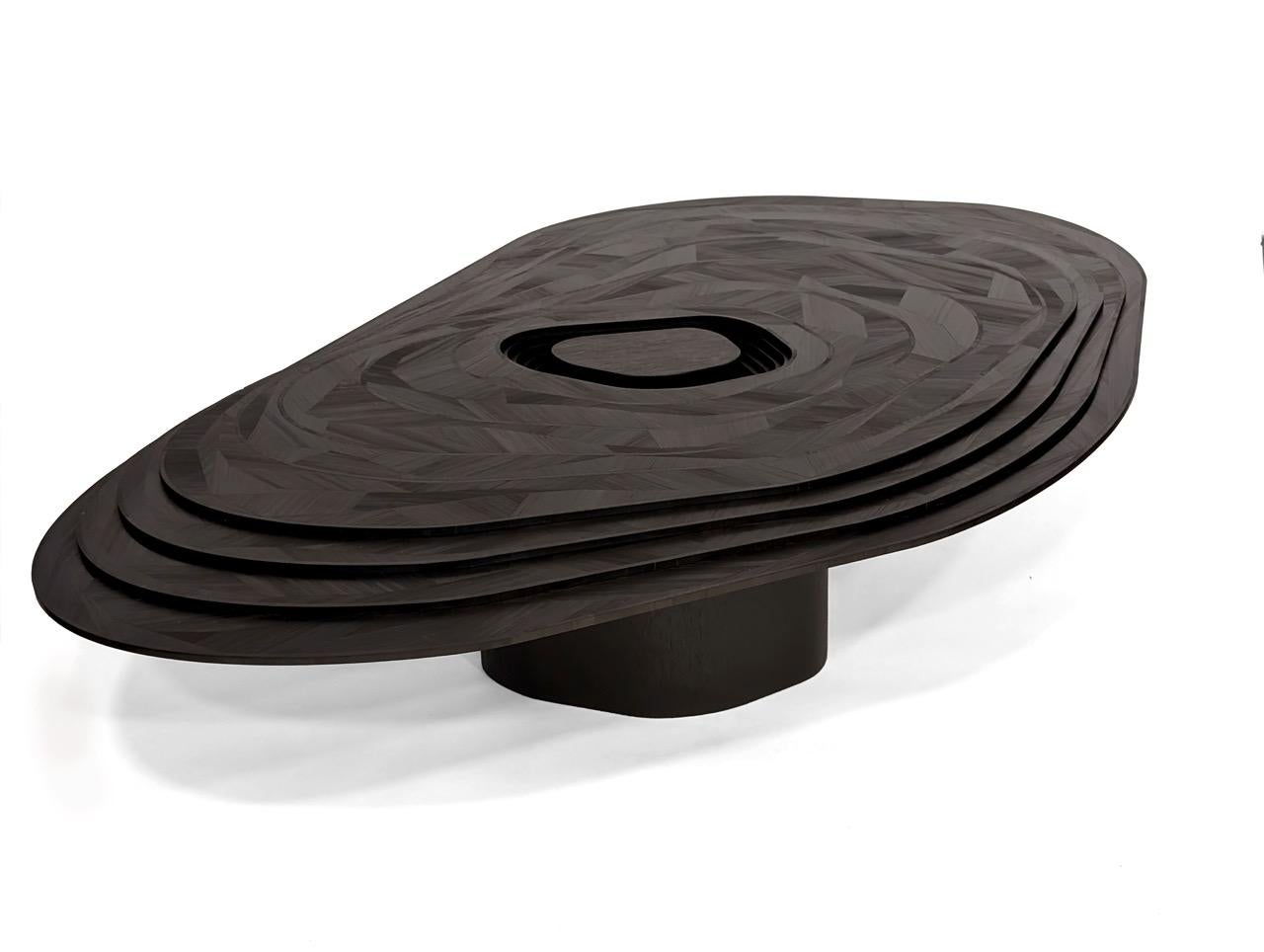 Tabla topográfica
Inspirada en los estratos geológicos, Topo es una mesa de centro escultórica que evoca el movimiento perpetuo mediante un juego de trampantojos entre el grosor real y las zonas planas de paja de centeno negra. En un monocromo