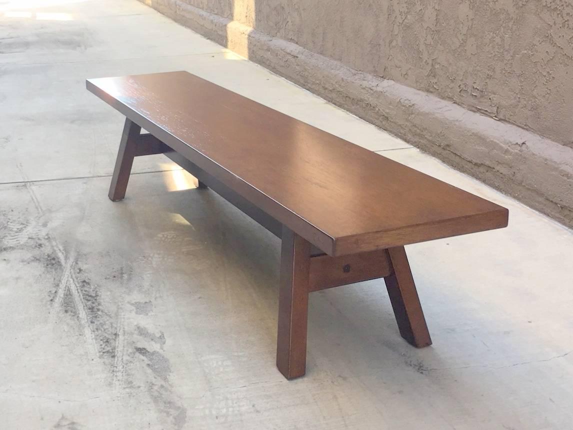 Walnut bench form with four splayed legs and trestle support.