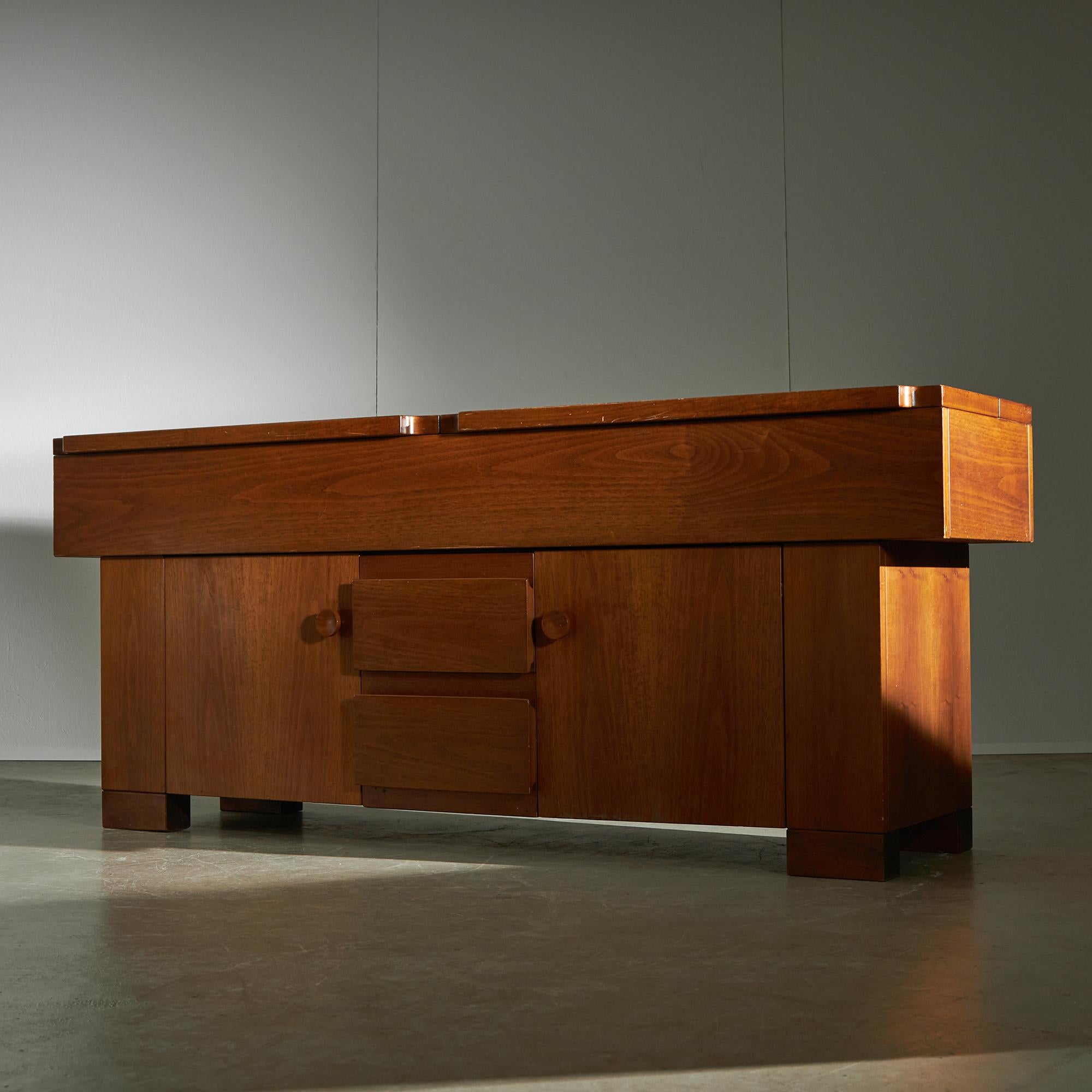 Credenza Torbecchia, in noce massiccio impiallacciato, con due ante a battente (con ripiani interni) e due cassetti nella parte anteriore, e un contenitore sotto il piano apribile. Il lato del mobile riporta la firma del designer Giovanni