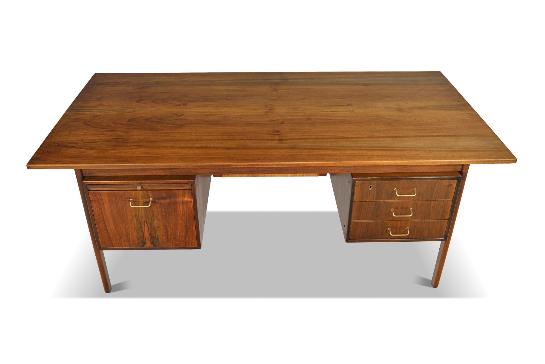 This remarkably well- preserved Danish modern executive desk was designed by Torben Strandgaard in the 1960s. This large walnut desk features a pull out writing tray, bank of drawers, and deep cabinet drawer. Adorned with original hand woven privacy