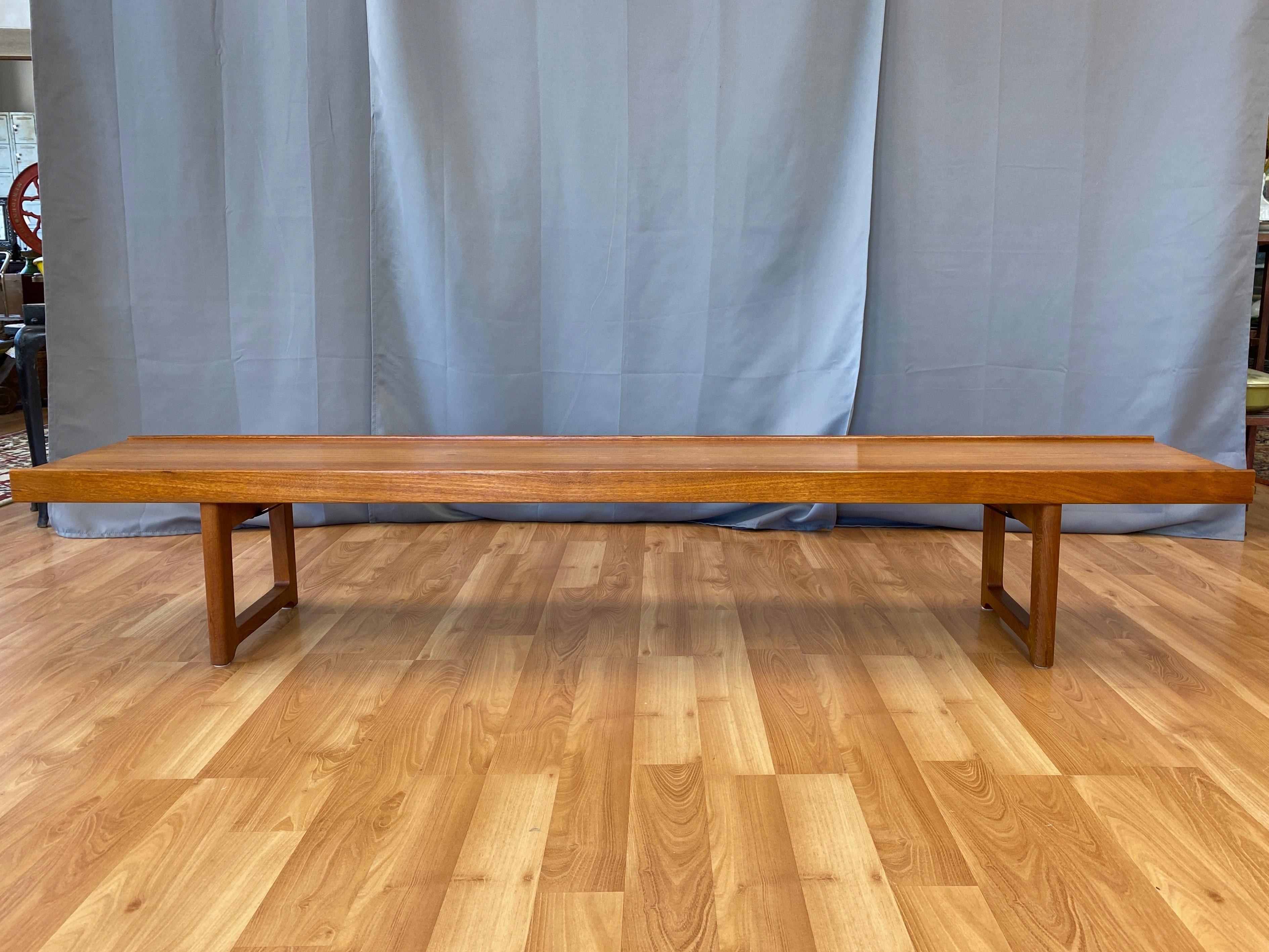 An expansive 1950s Scandinavian Modern “Krobo” low teak bench or coffee table by Torbjørn Afdal for Mellemstrands Trevareindustri and produced by Bruksbo.

Freshly refinished top with golden, subtly figured bookmatched teak that's a bit darker