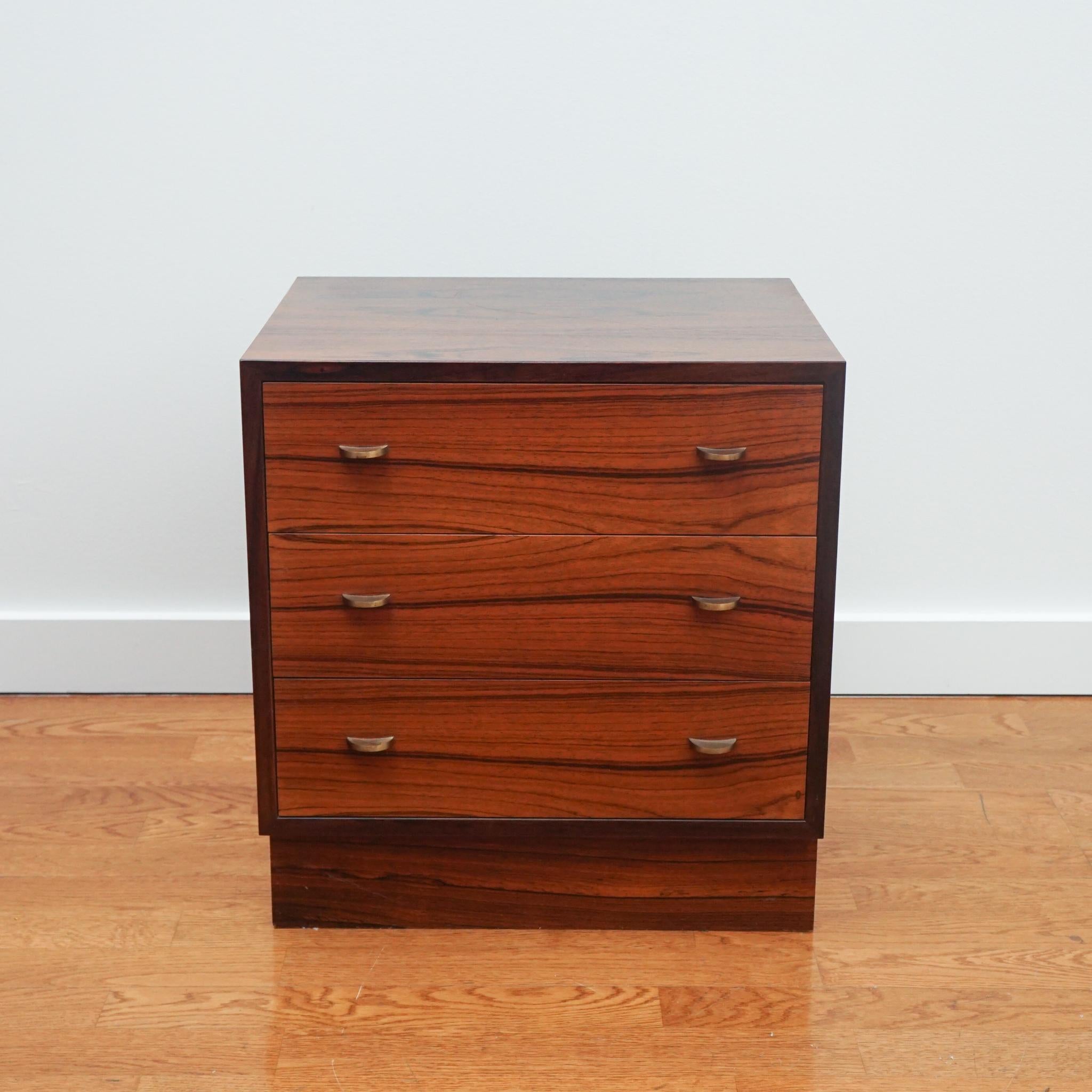 The handsome three-drawer chest of drawers, shown here, was designed by Torbjørn Afdal for Bruksbo in 1950s. Made of rosewood, each drawer is distinguished by dove-tail joinery and carved wood glides. Flat, half-moon shaped brass pulls complement