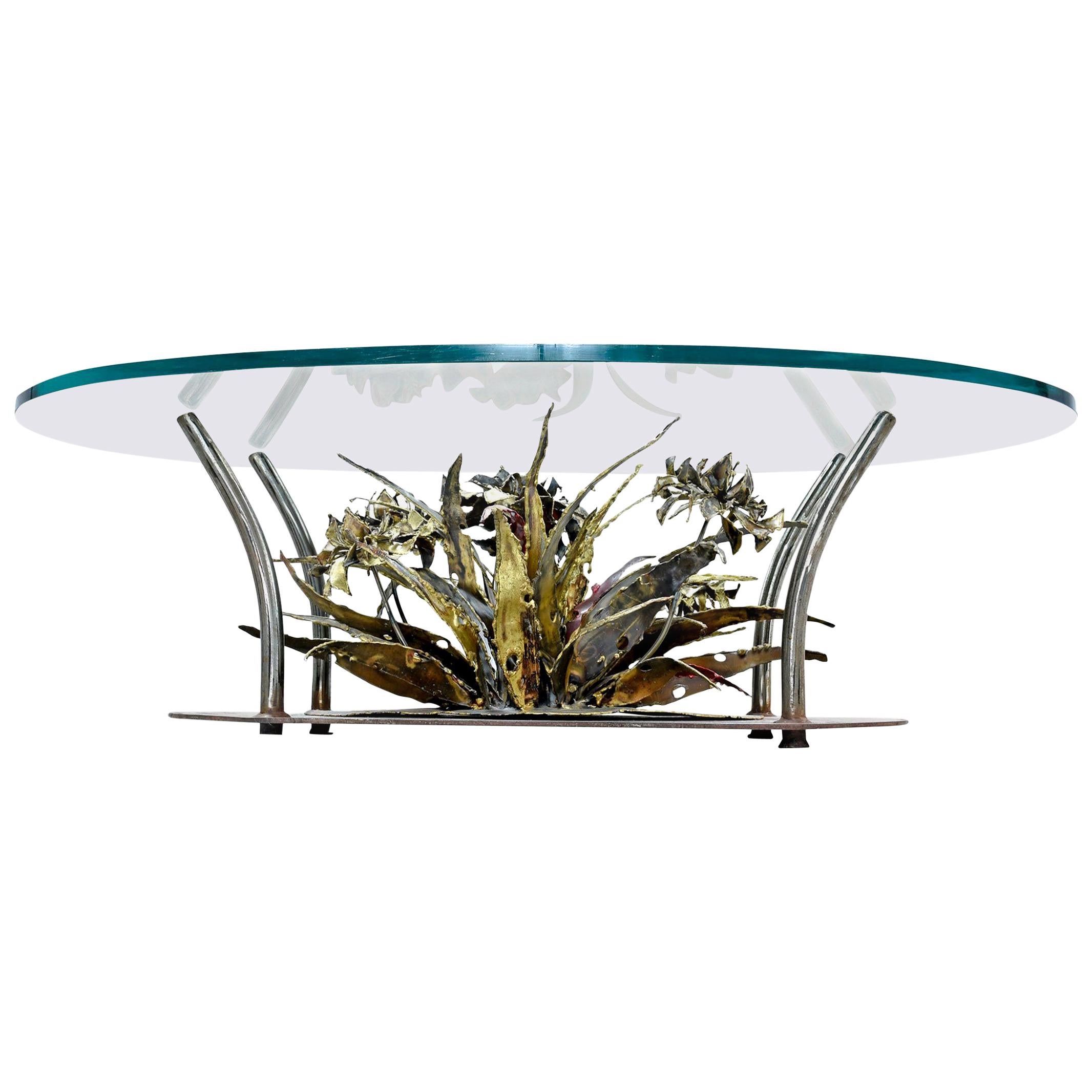 Brutalist Mid-Century Modern coffee table by Silas Seandel. The undulating oval shaped base features a large, organic floral sculpture made of patinated metal with copper, steel, gold and brass tones. The base is topped with a thick oval shape glass