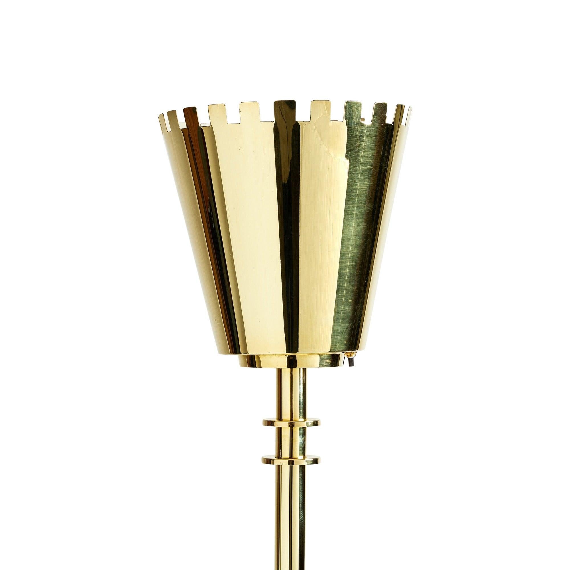 Lampadaire en laiton de style torchère comprenant un abat-jour en forme de vase avec un bord supérieur crénelé, monté sur une tige verticale supportée par deux disques sur une base circulaire. ?