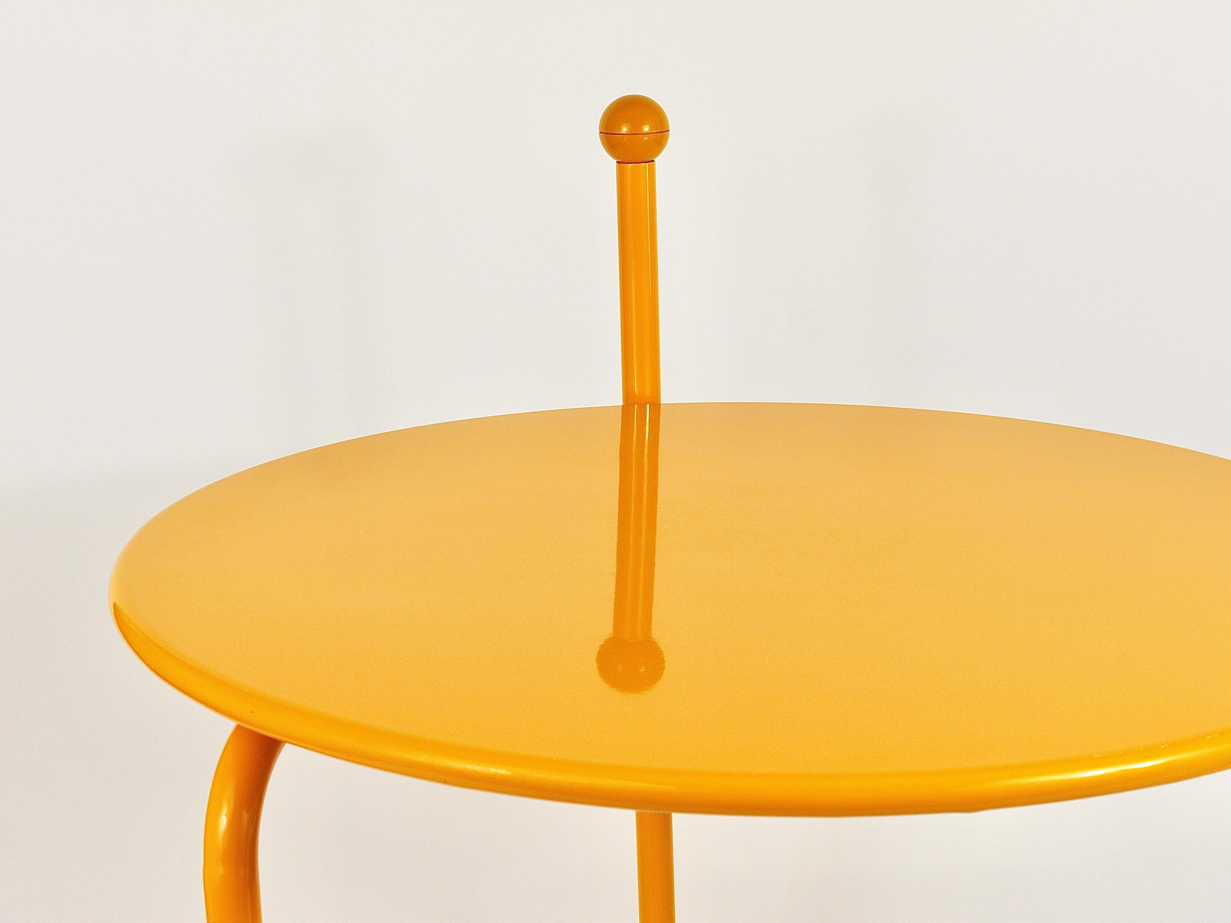A round folding Memphis style coffee / side / occasional flip-top table in yolk-yellow. Designed in 1986 by Tord Björklund for Ikea. This collapsible table is made of metal, has lovely round castors and a nice handle with a yellow ball on its top to