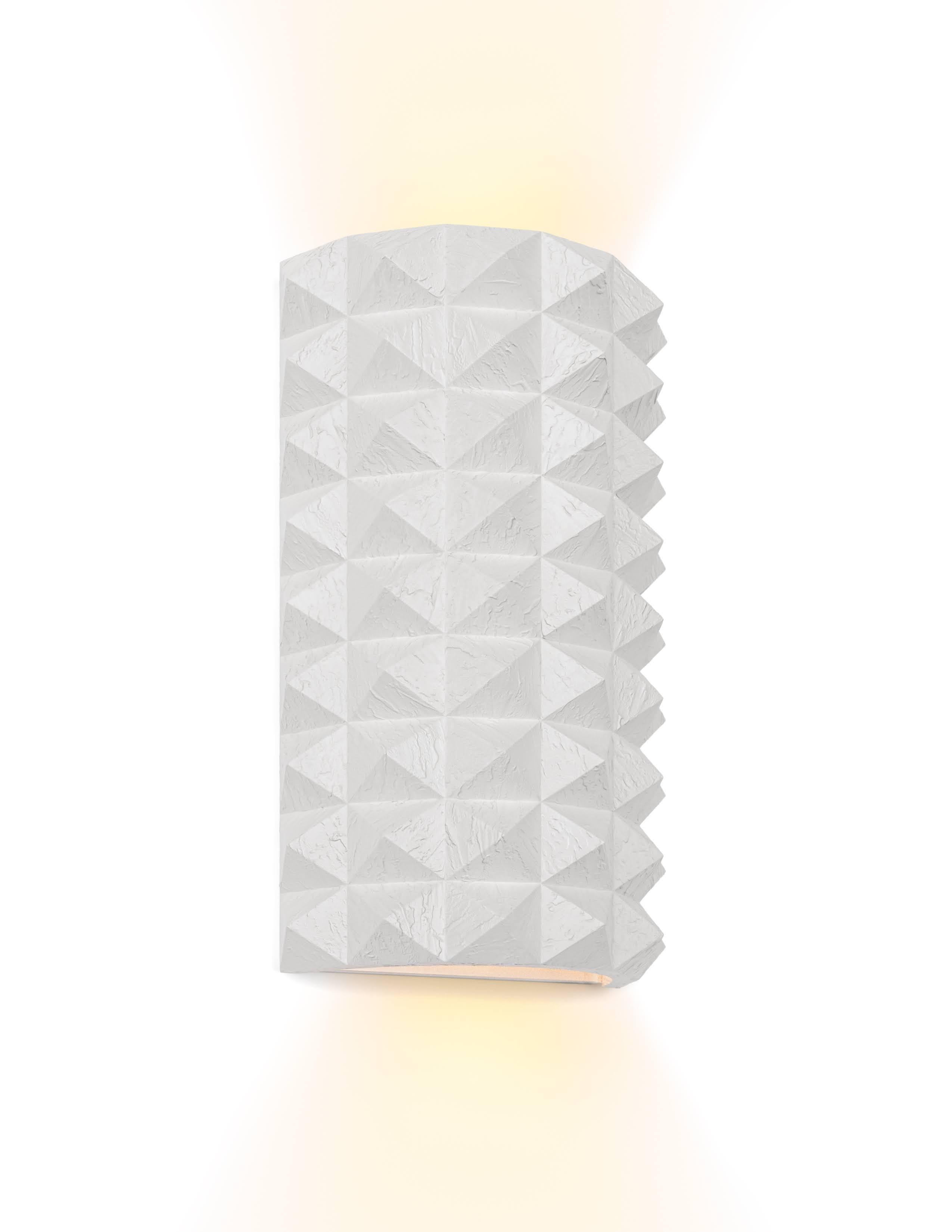Elegant and architectural, the Toria Wall Sconce by Brian Chaaban brings a refined sense of balance and materiality to any interior. A central metal bracket anchors a hand-finished glass cylinder, emitting a soft glow that complements both modern