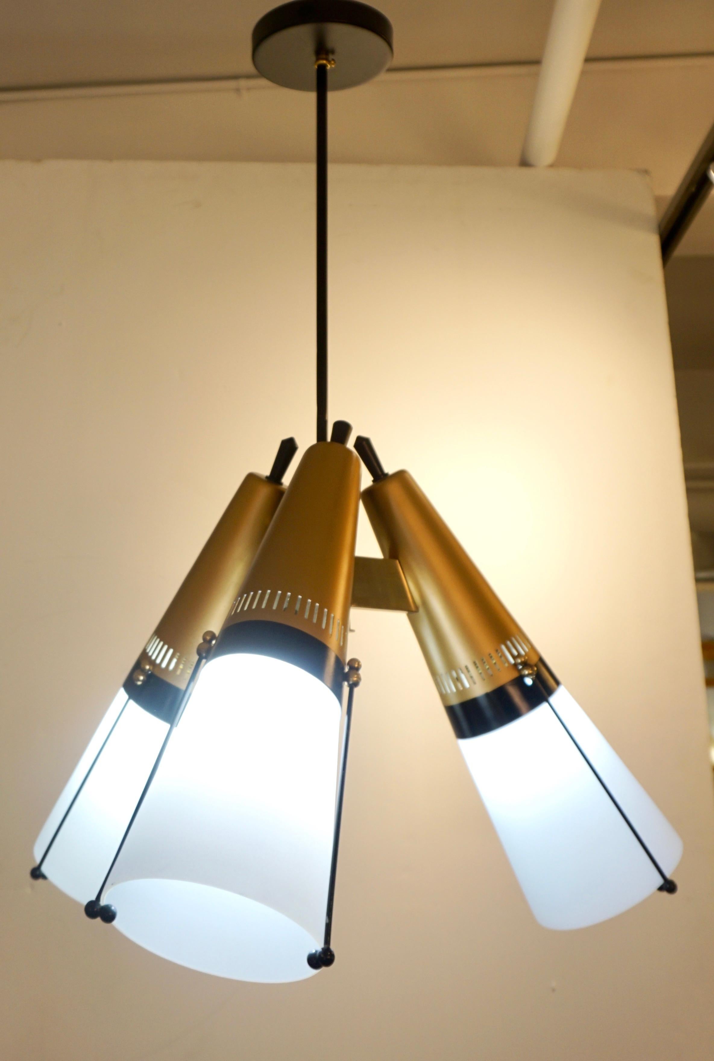 A 1950s delightful 3-light modern design pendant chandelier attributed to the Italian designer Oscar Torlasco. Three cones in white glass, enclosing the light source and ending in a perforated metal upper part, cold painted in matt gold brass color,