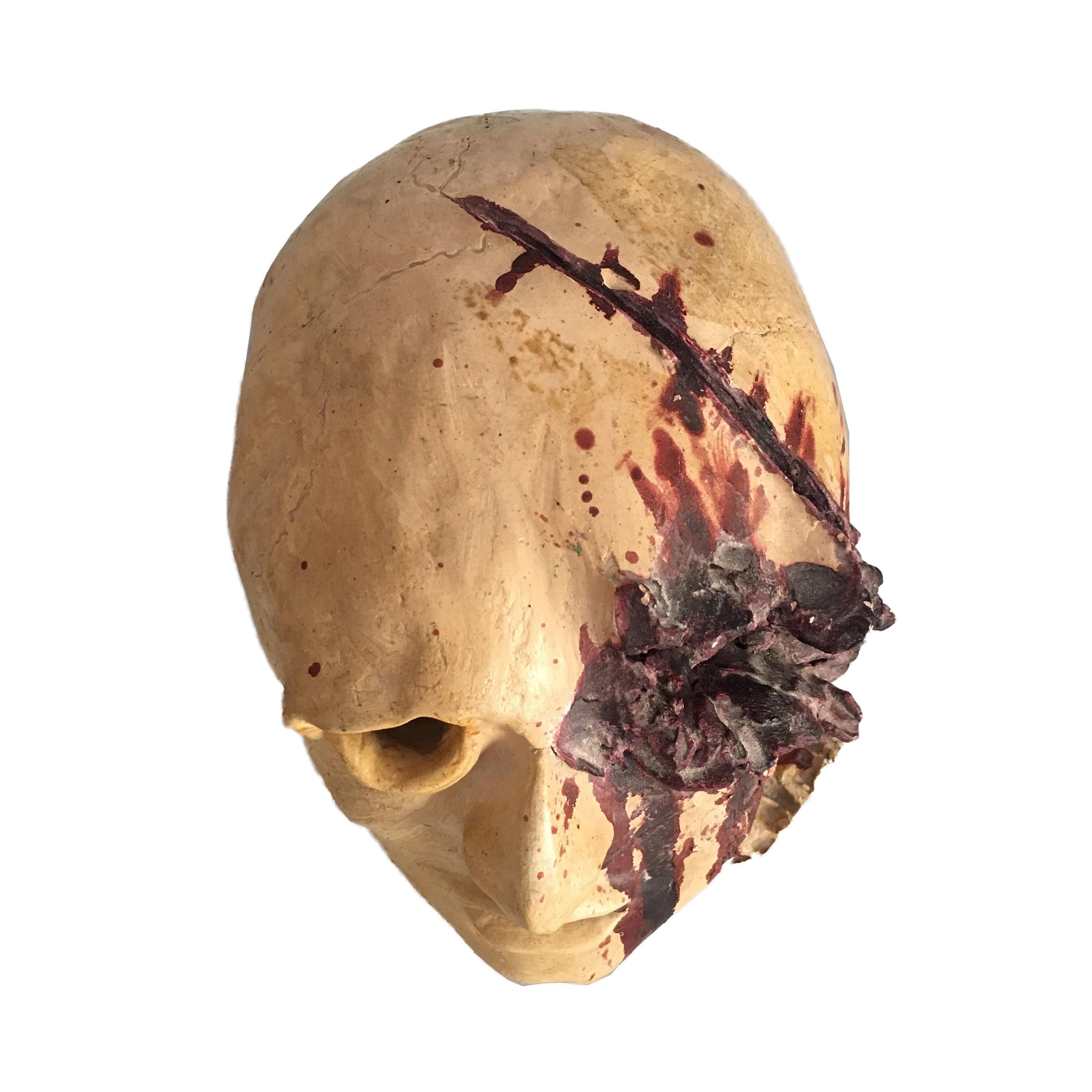Diese Skulptur ist aus Keramik und stellt einen menschlichen Kopf dar, der durch einen Axthieb zerrissen wurde, was die Wunde bluten lässt. Das Blut fließt in die rechte Gesichtshälfte und erreicht das Auge.