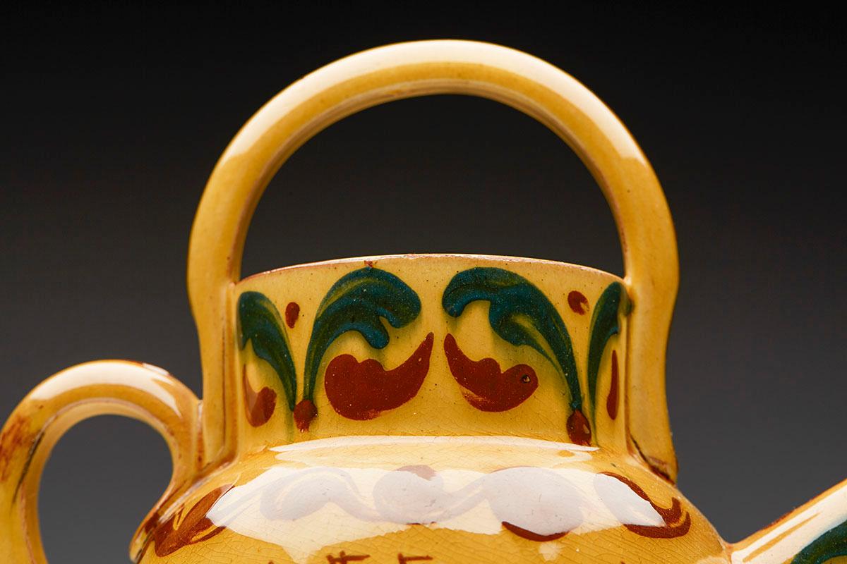 A stylish Arts & Crafts Torquay ware art pottery mottoware water jug decorated with the Kerswell Daisy pattern on a mustard yellow ground and dating from around 1890. The jug has an enclosed pouring spout and both a carrying and side pouring handle