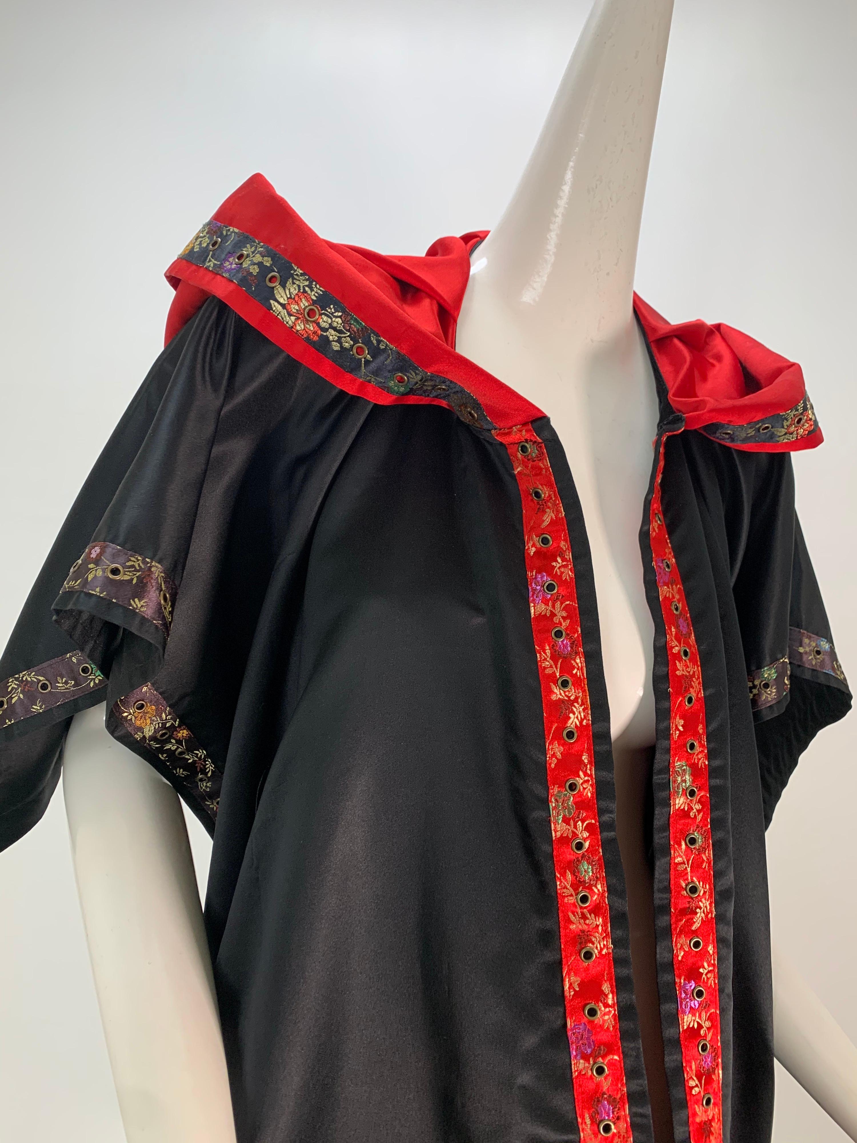 A Torso Creations black and red silk satin hooded wrap stole trimmed in brocade tape and brass eyelets. Large patch pockets at both ends. Free size.