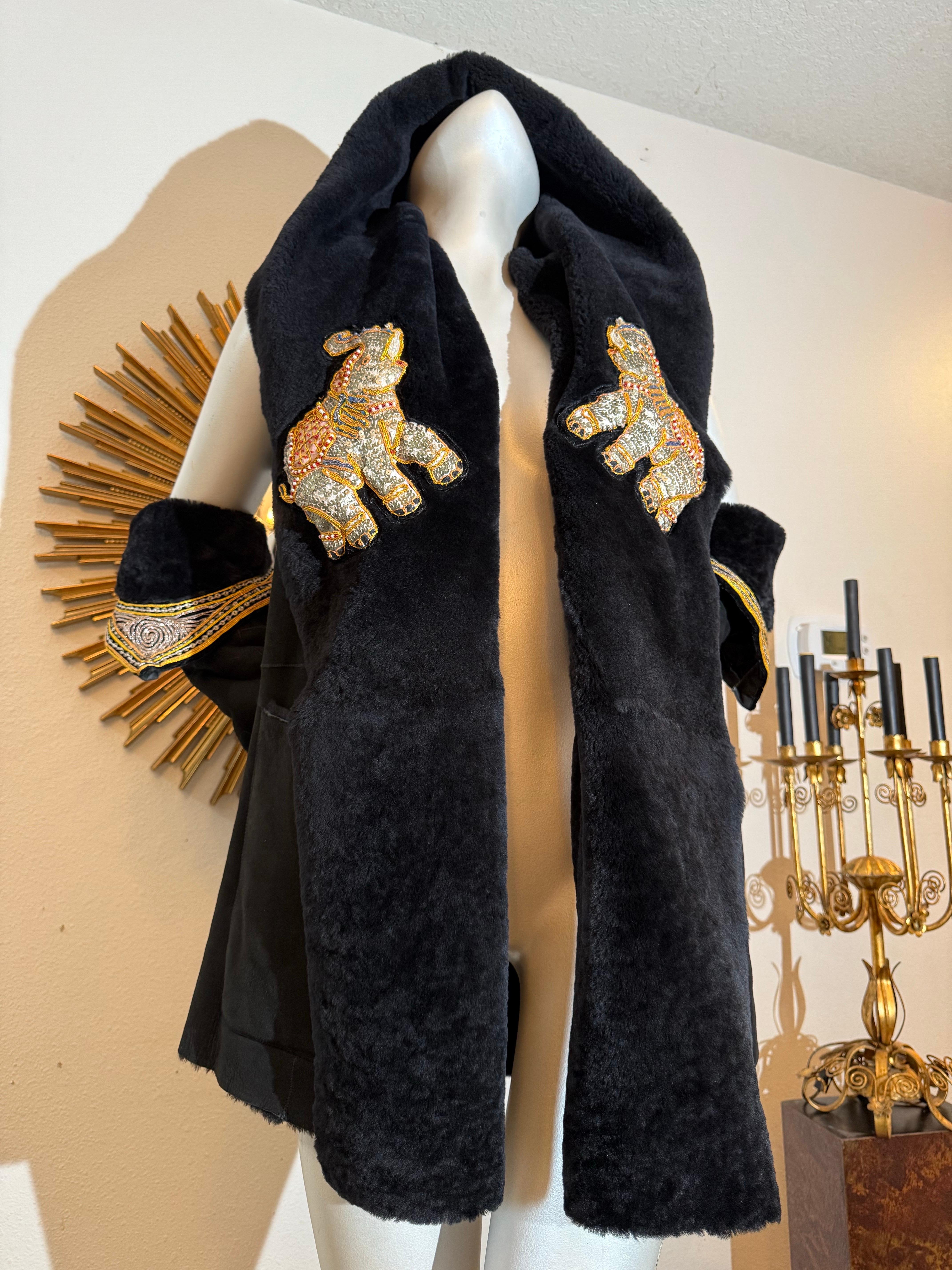 Torso Creations - Ensemble gilet à capuche et gantelet en shearling noir avec broderie d'éléphant :  Cette pièce polyvalente peut être portée comme un col châle ou une capuche. Il est orné de spectaculaires figures traditionnelles indiennes