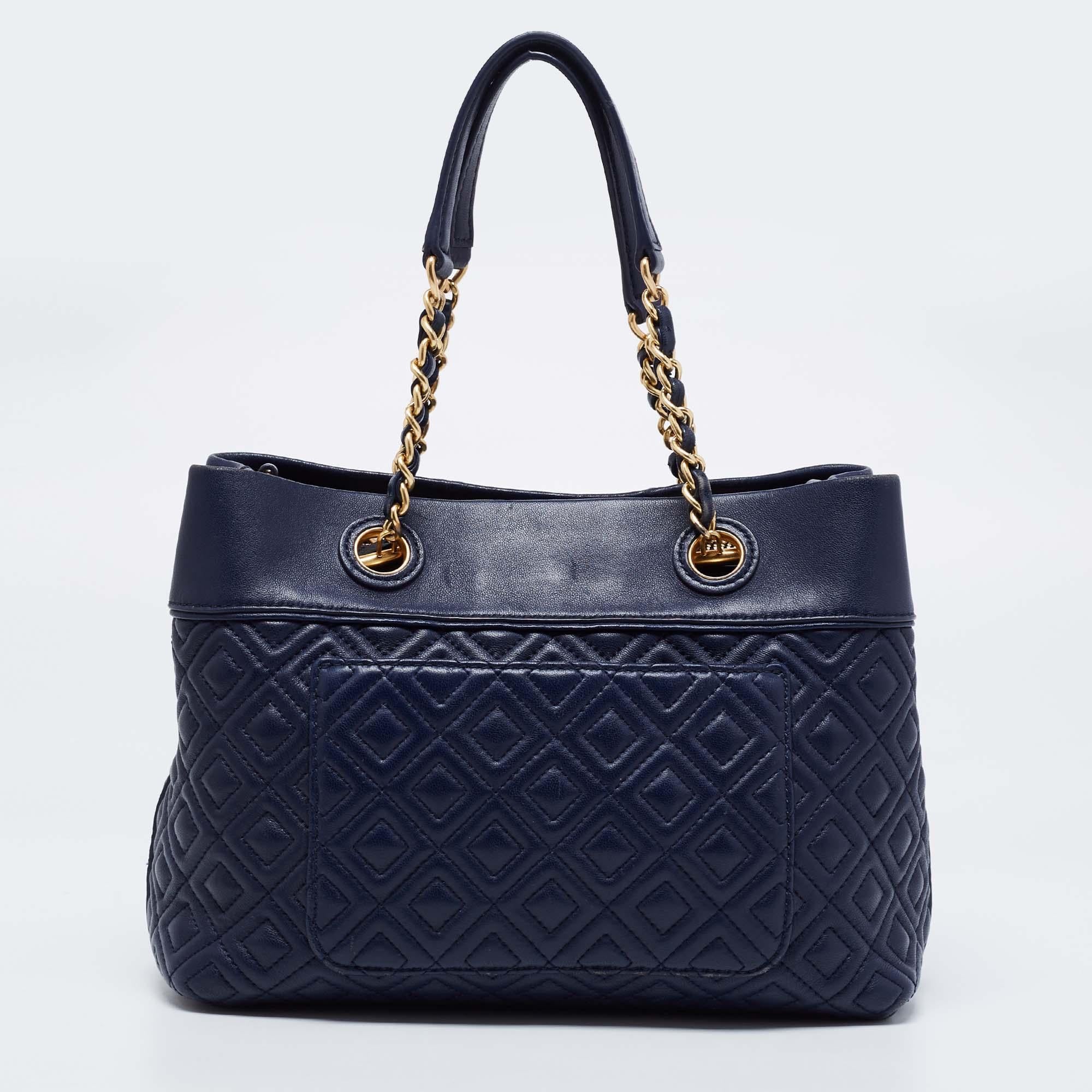 This Fleming tote from Tory Burch has been meticulously crafted from leather in a classy blue hue and designed with quilts in diamond patterns and the logo on the top. It has a fabric-lined interior, shoulder handles, and an ooptional strap. This is