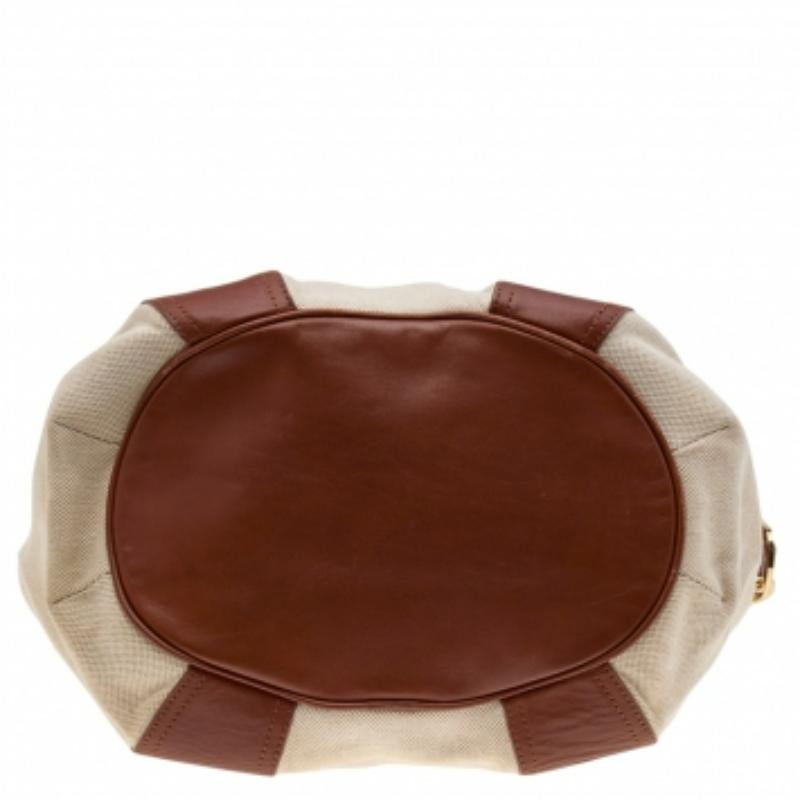 Give your outfit an instant boost with this graceful canvas and leather handbag by Tory Burch. The brown-beige bag is lined with fabric and keeps your essentials safe. It features two handles and a shoulder strap, gold-tone hardware, and drawstring