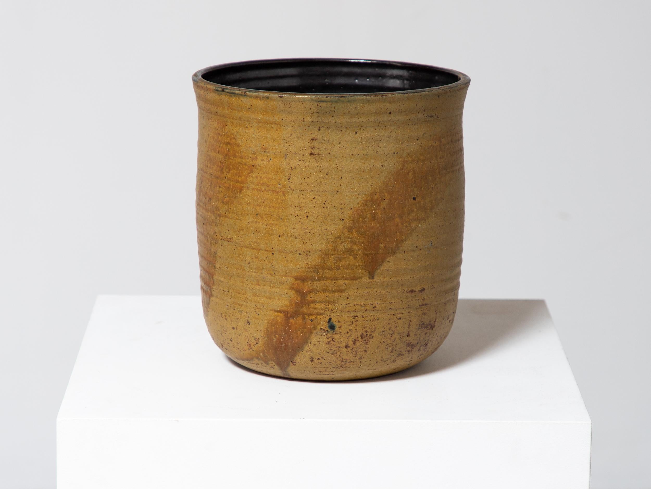 Early vase by renowned Japanese American ceramicist Toshiko Takaezu. This handmade vessel features a soft, rounded form with a wide opening, and a rich palette earthtones in ochre, mustard, and deep black within the interior. The artist's hand is