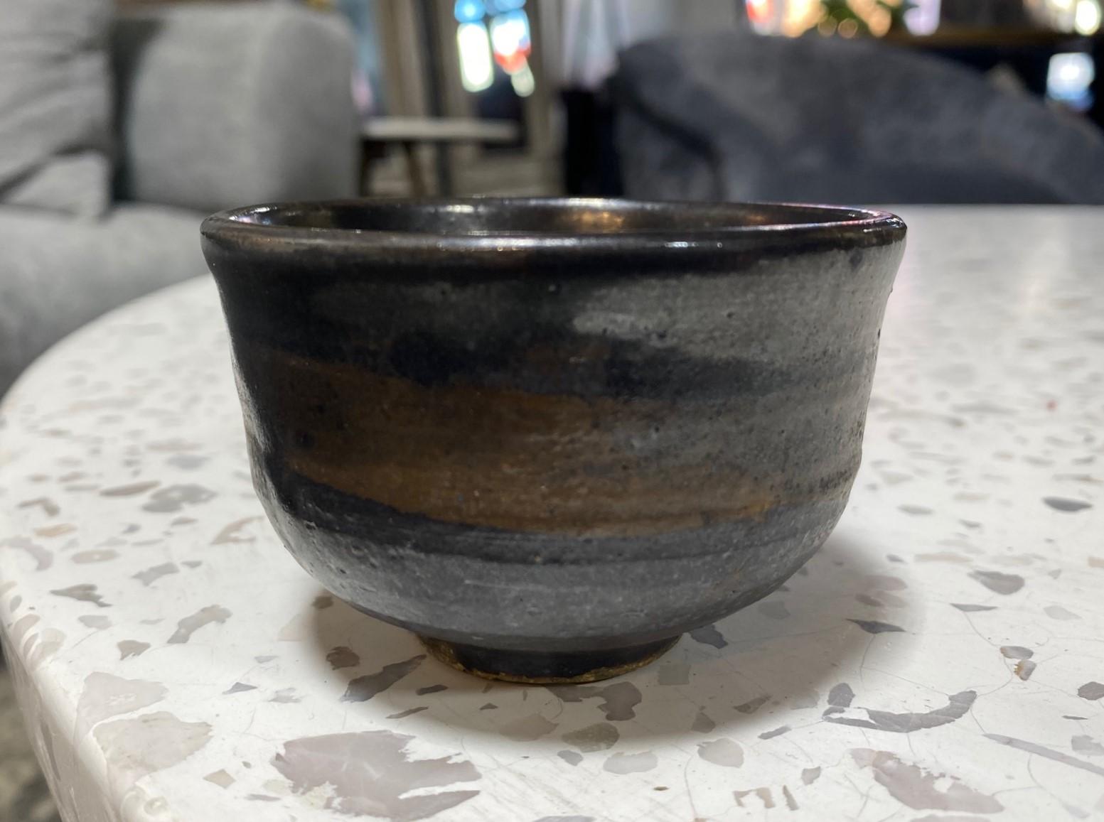 An absolutely gorgeous and wonderful chawan tea bowl / yunomi cup by famed Japanese American pottery master Toshiko Takaezu. The work features a rich, matte black tenmoku glaze with splashes of brushed colors. It is a unique and one-of-a-kind work