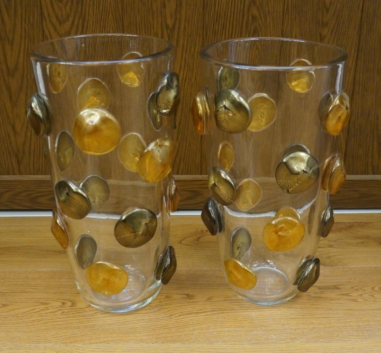 Two Murano glass blown vases, clear color with amber/gold and black/gold buttons.
The vases are of thick glass.
Project by Toso Murano in 1995s
Vases signed with engraving: Toso Murano

An original Murano glass vase represents the symbol of an