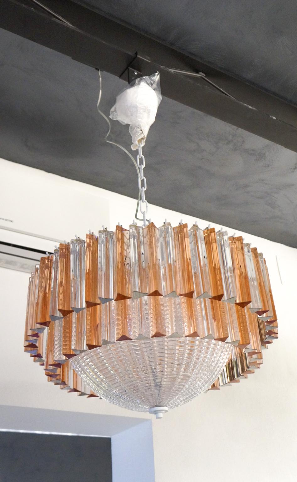 Murano blown glass chandelier with 95 crystal and rose elements, white frame and central part in crystal glass.
The elements of this typical chandelier are called Triedri, for its triangular shape. 
The assistants take a small quantity of glass