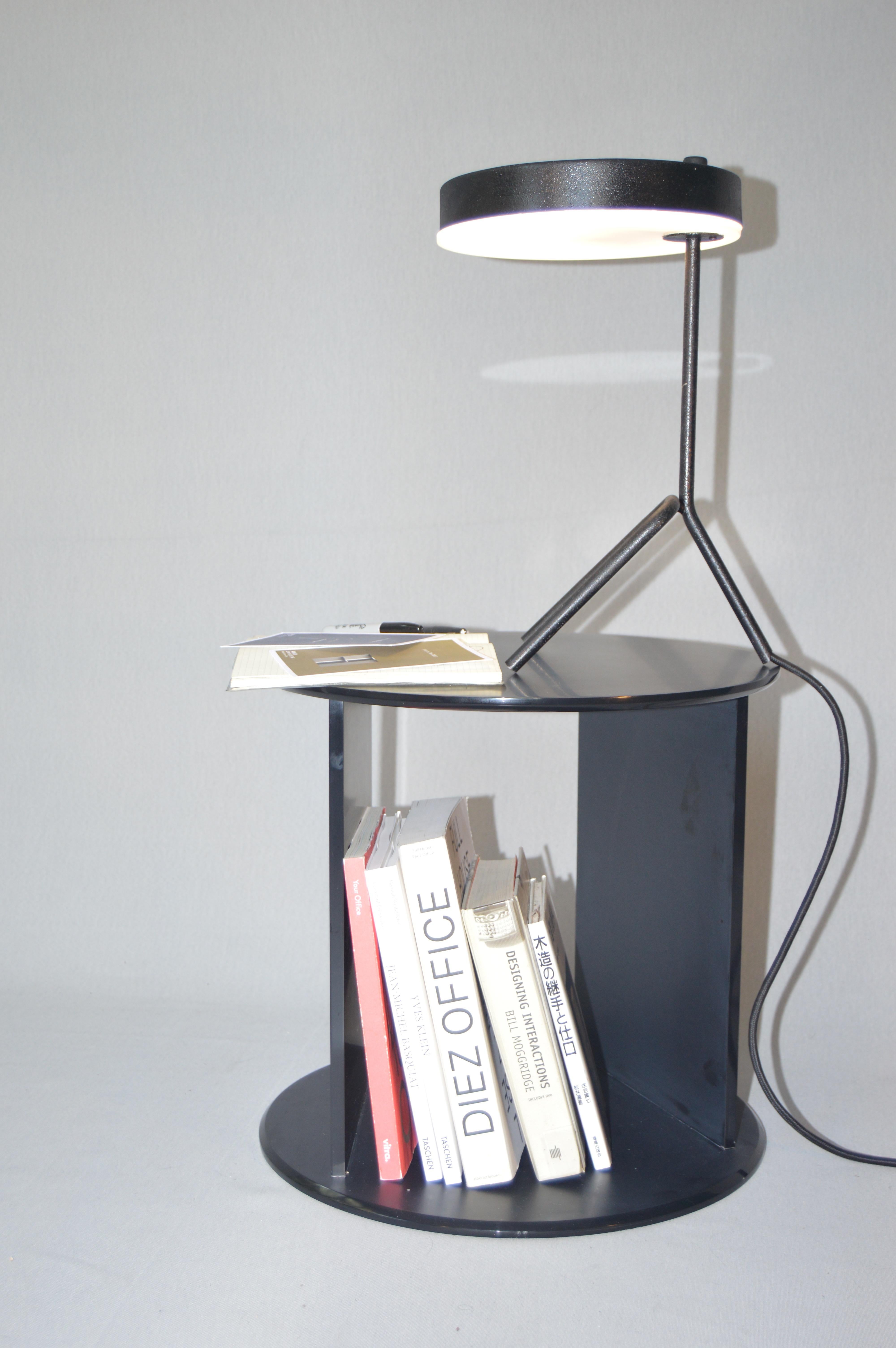 Totem est une table d'appoint cylindrique creuse, construite à partir d'éléments simples. Une partie du charme de la pièce réside dans le contraste entre les faces opaques de la finition et un fond de verre.  bord poli, renforçant la noblesse du