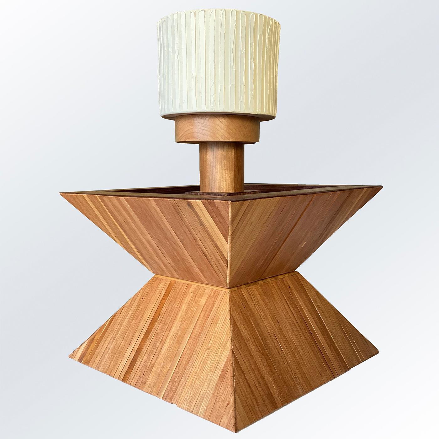 Featuring a sculptural cherry body consisting of two truncated pyramids sealed together and marked by thin grooves, this table lamp is a singular piece entirely handcrafted, numbered, and signed by the artist. The topping shade in off-white ceramic