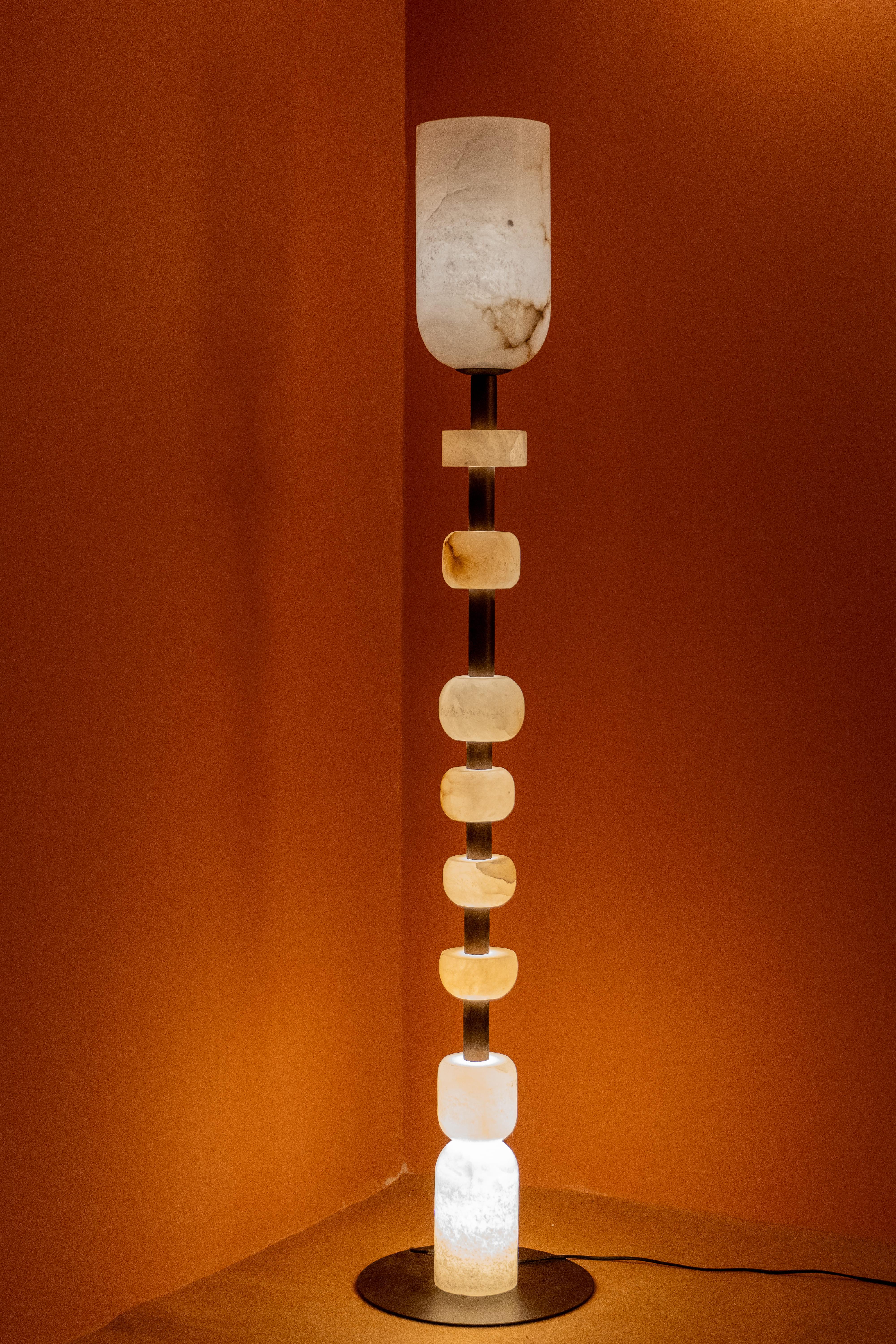 Elevate your interior with this sculptural floor lamp, a stunning fusion of art and illumination. Crafted with stacked alabaster, stain-less steel & Wood, each segment glows warmly when lit, casting a soft, ambient light that enhances any space with