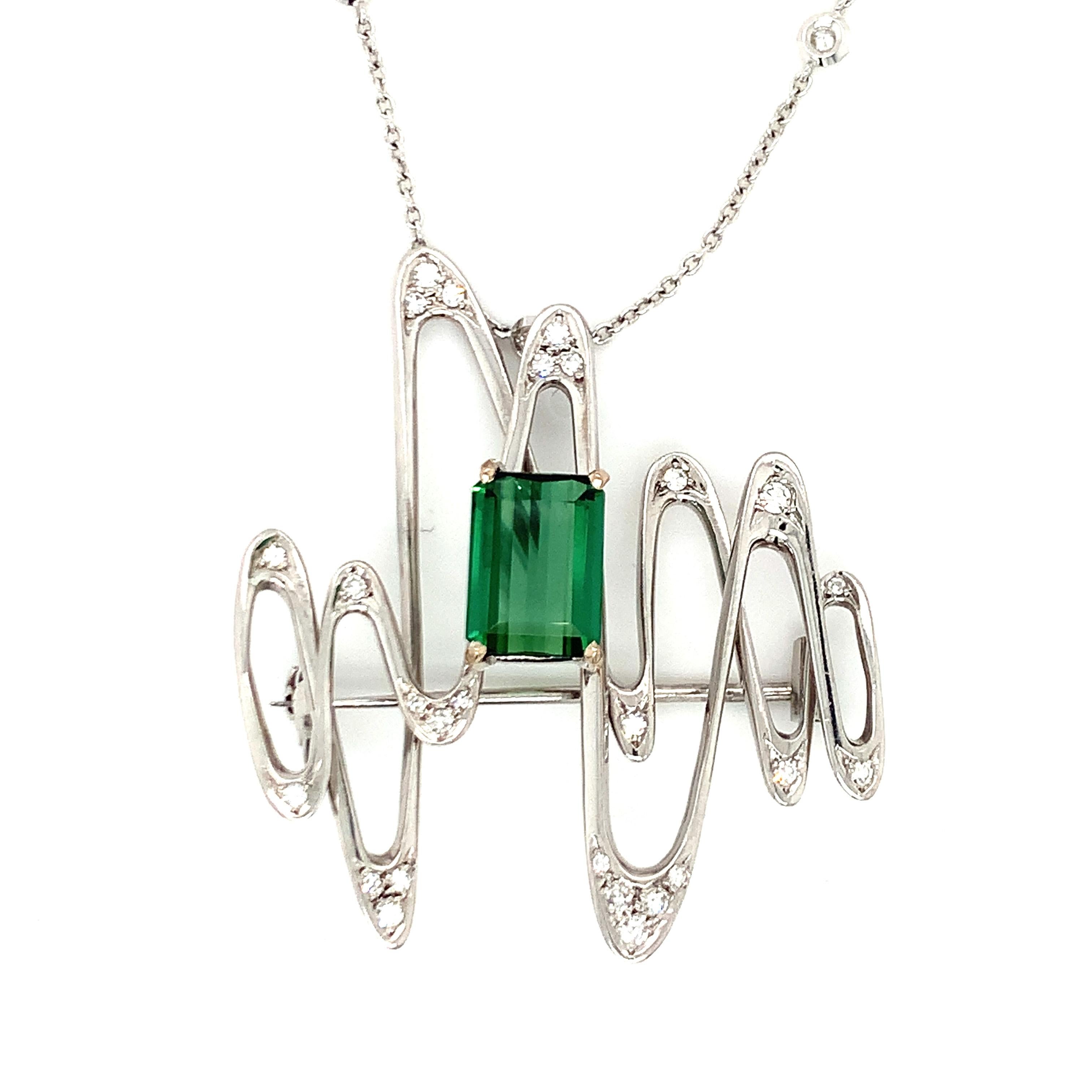 One green tourmaline and diamond 18K white gold brooch / pendant featuring an abstract design centering one emerald cut, green tourmaline weighing 3.50 ct. with 27 round brilliant diamond accents totaling 0.30 ct. Attached to an 18K white gold