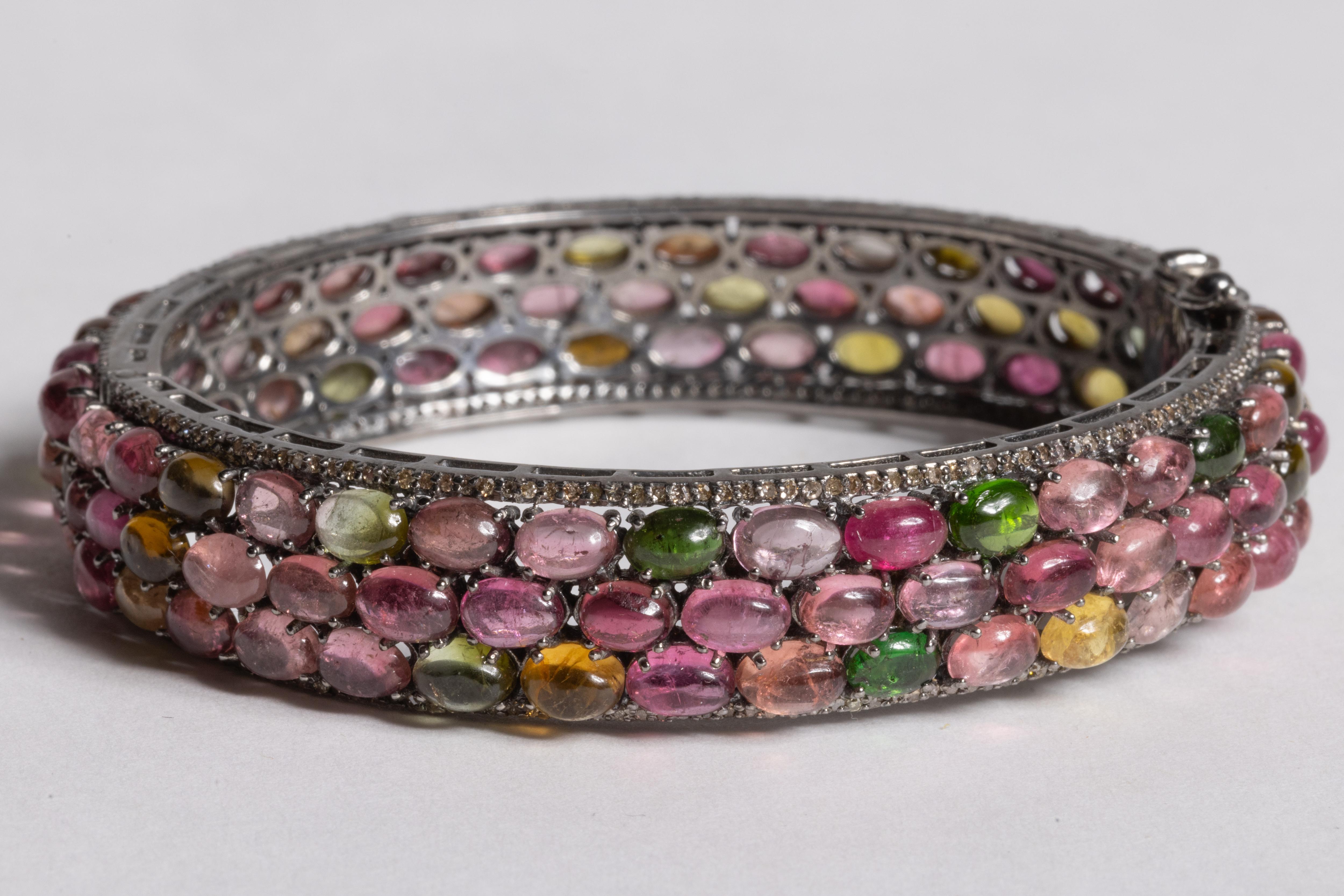A lovely bangle bracelet with three rows of cabochon multi colored, oval tourmalines bordered with pave`set diamonds.  Predominant tourmalines are the coveted pink.  All set in an oxidized sterling silver.  Inside circumference is 7