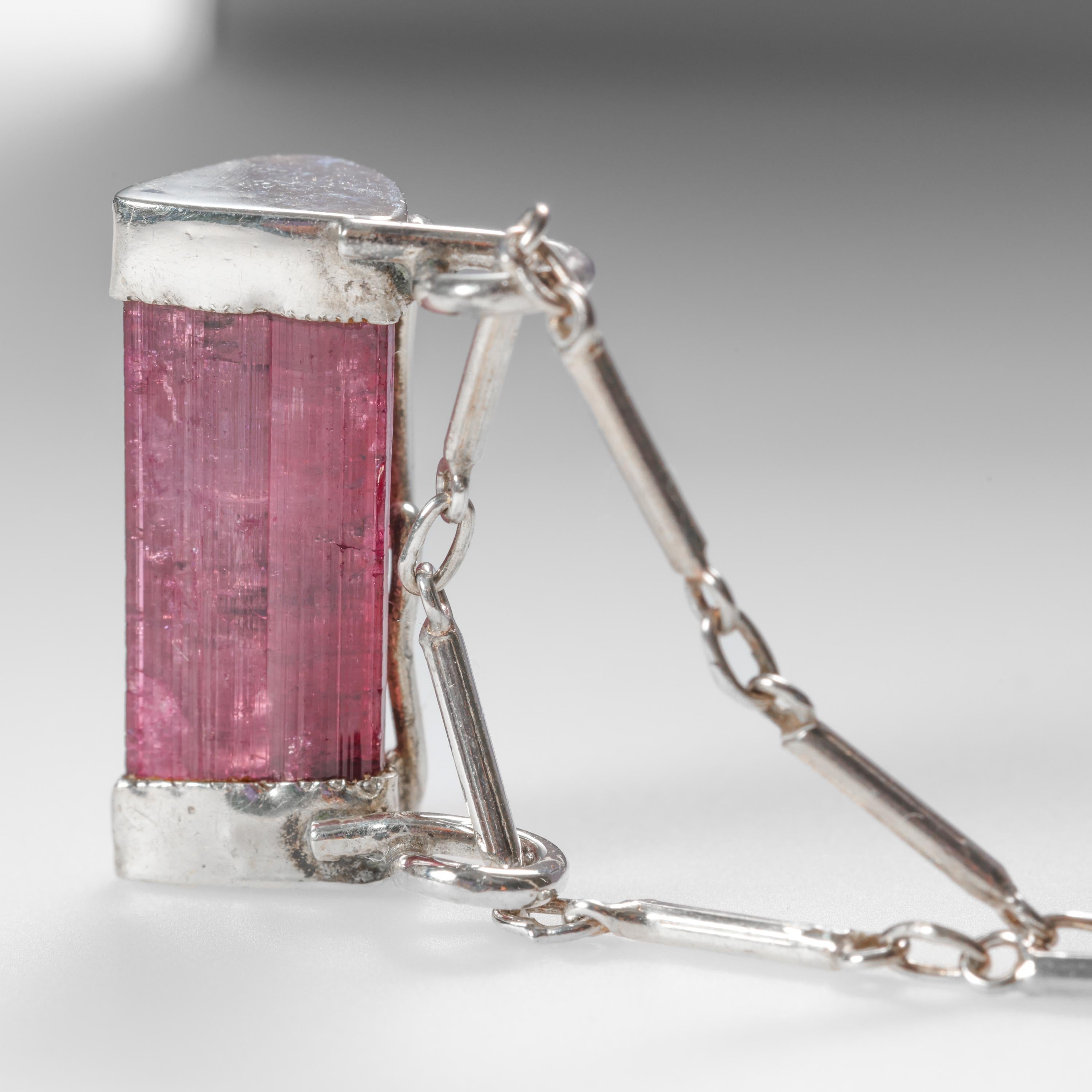 This circa 1960s silver choker pendant necklace features a natural, raw raspberry tourmaline crystal set into a custom-fabricated silver mounting. The silver-enclosed tourmaline pendant measures 22.63mm x 8.48mm not including the double loops at