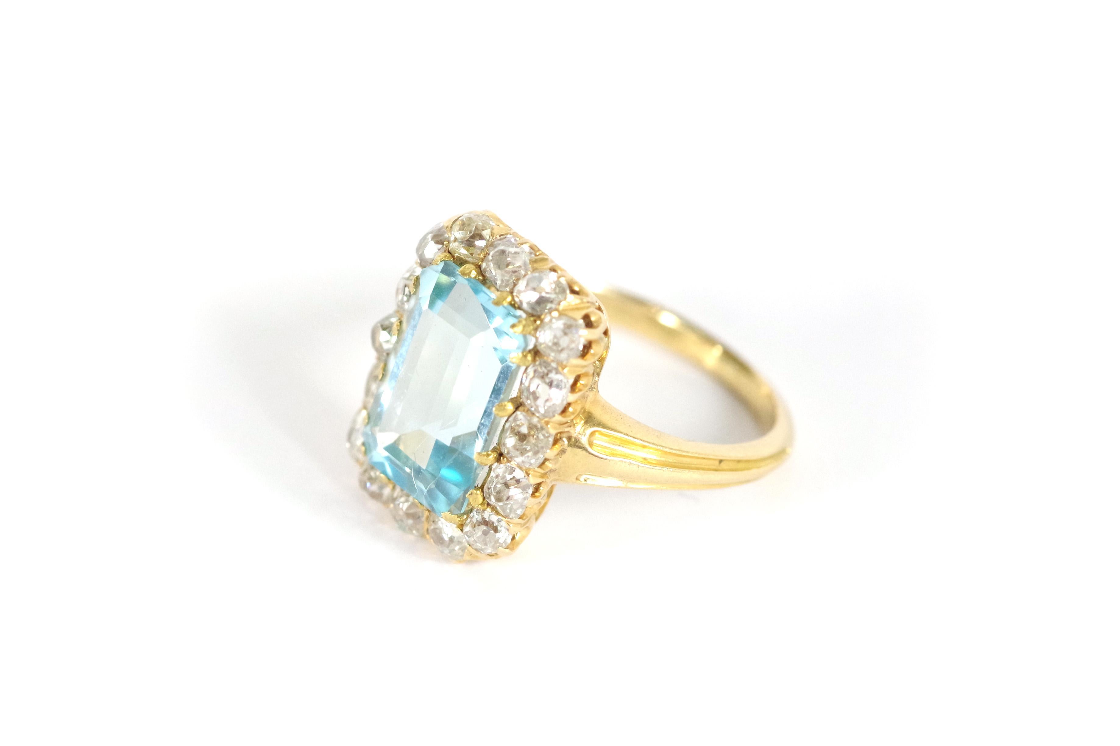 Blue topaz diamond ring in 18 karat yellow gold. Antique ring with a large rectangular-cut ice blue topaz in a setting of 16 old-cut diamonds. The stone has a lovely crystalline blue color very similar to an aquamarine stone. Antique cluster ring