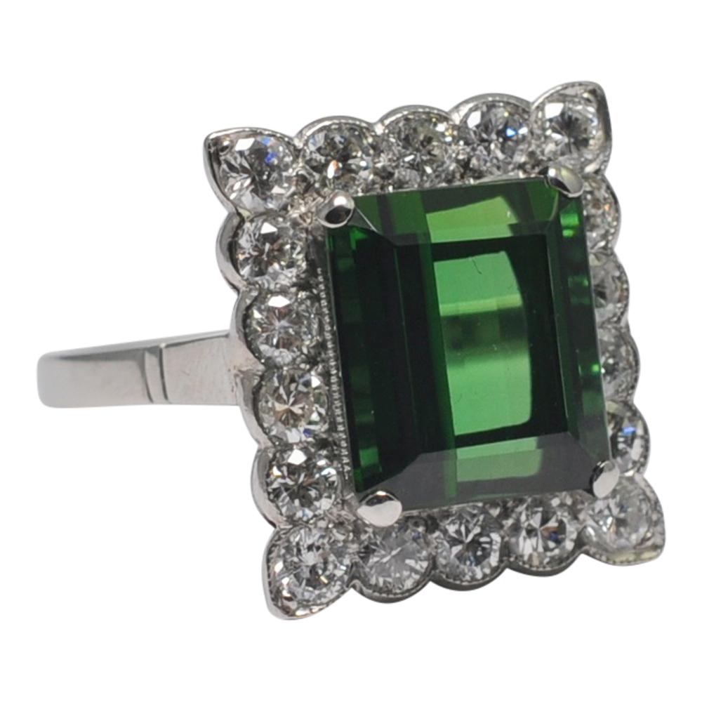 Dramatic and bold green tourmaline and diamond ring set in platinum; the emerald cut tourmaline is a rich deep green and weigh 5.36ct.  It is set with 4 claws and surrounded by brilliant cut diamonds totalling 1.44ct in a millegrain setting.  The