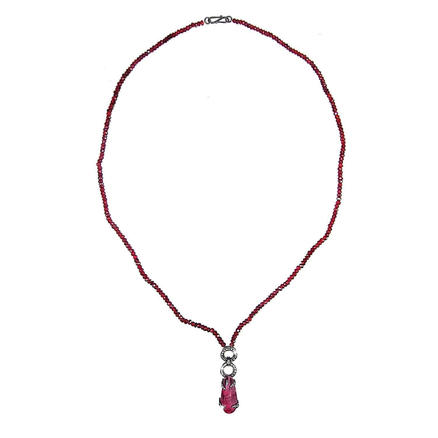 A beautiful natural pink tourmaline and diamond pendant suspended by two circular diamond links set in blackened oxidized silver on a chain of natural blood red garnets.
- Pendant is pink cabochon accented with single cut white diamonds 
- Suspended