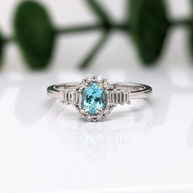 This gorgeous blue Afghan tourmaline ring is showcased in a custom NNJ ring design with two sizes of natural diamond accents that give an extra sparkle! With radiant diamonds surrounding a 5.5x4mm tourmaline, this piece is classy and