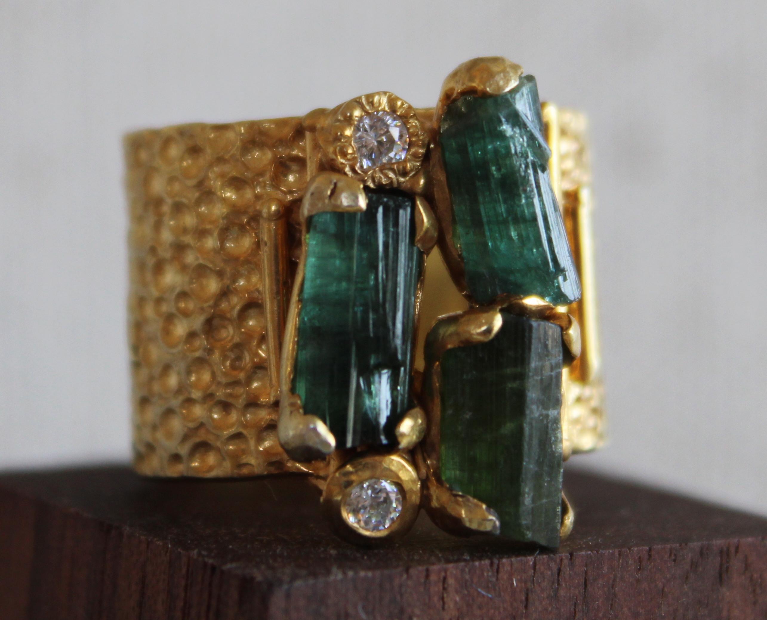 Three stone deep forest green raw cut tourmaline 14K gold plated over sterling silver cocktail ring. This ring features 3 raw cut vertically set tourmaline stones with two round topaz stones set above and below the tourmalines. The band is cast in