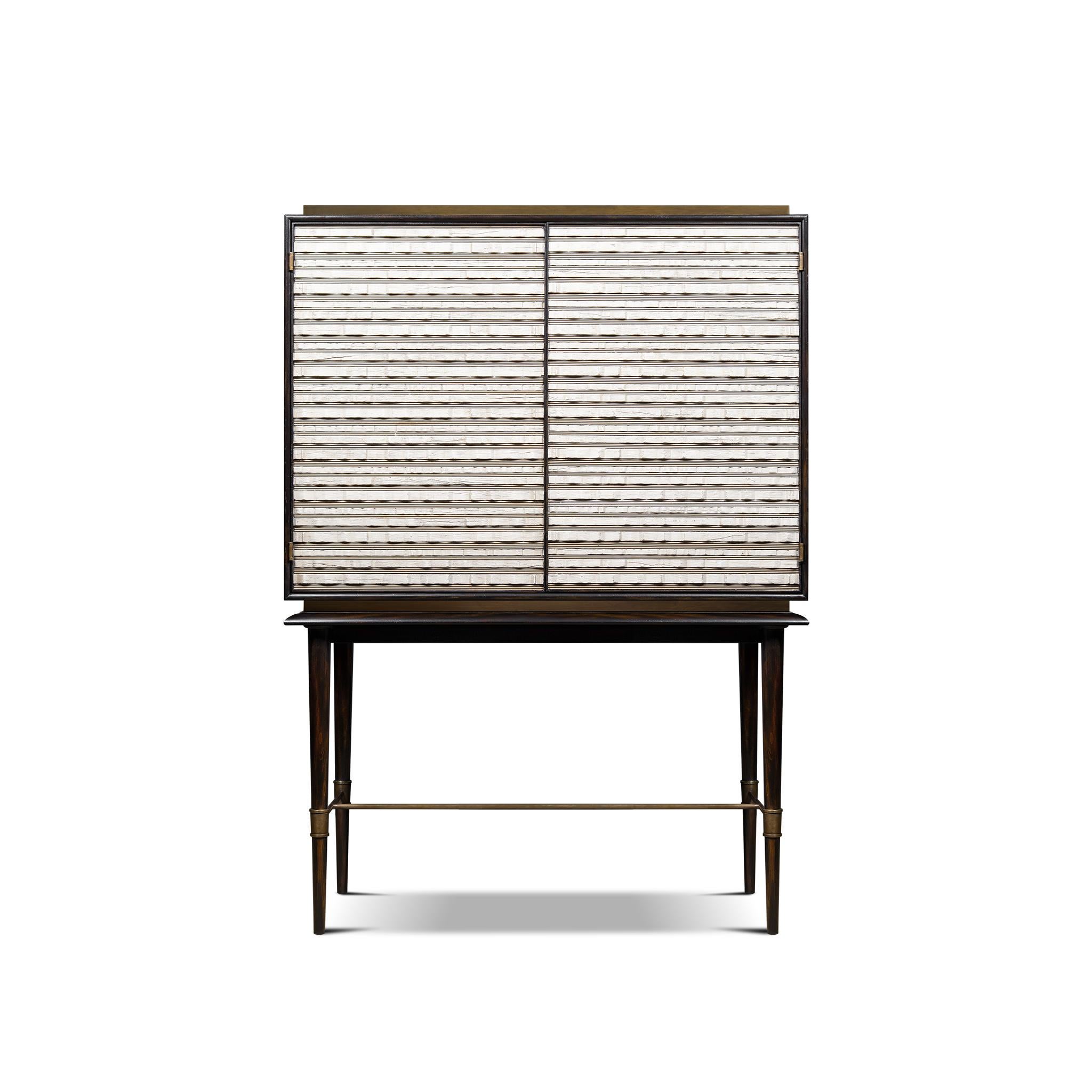 The Tourmont cabinet on stand was inspired by natural and irregular patterns found in mountainous rocks highlighted by a dark frame. The cabinet has a brass base and top which lies on an elegant stand that has delicate pointed legs with a brass