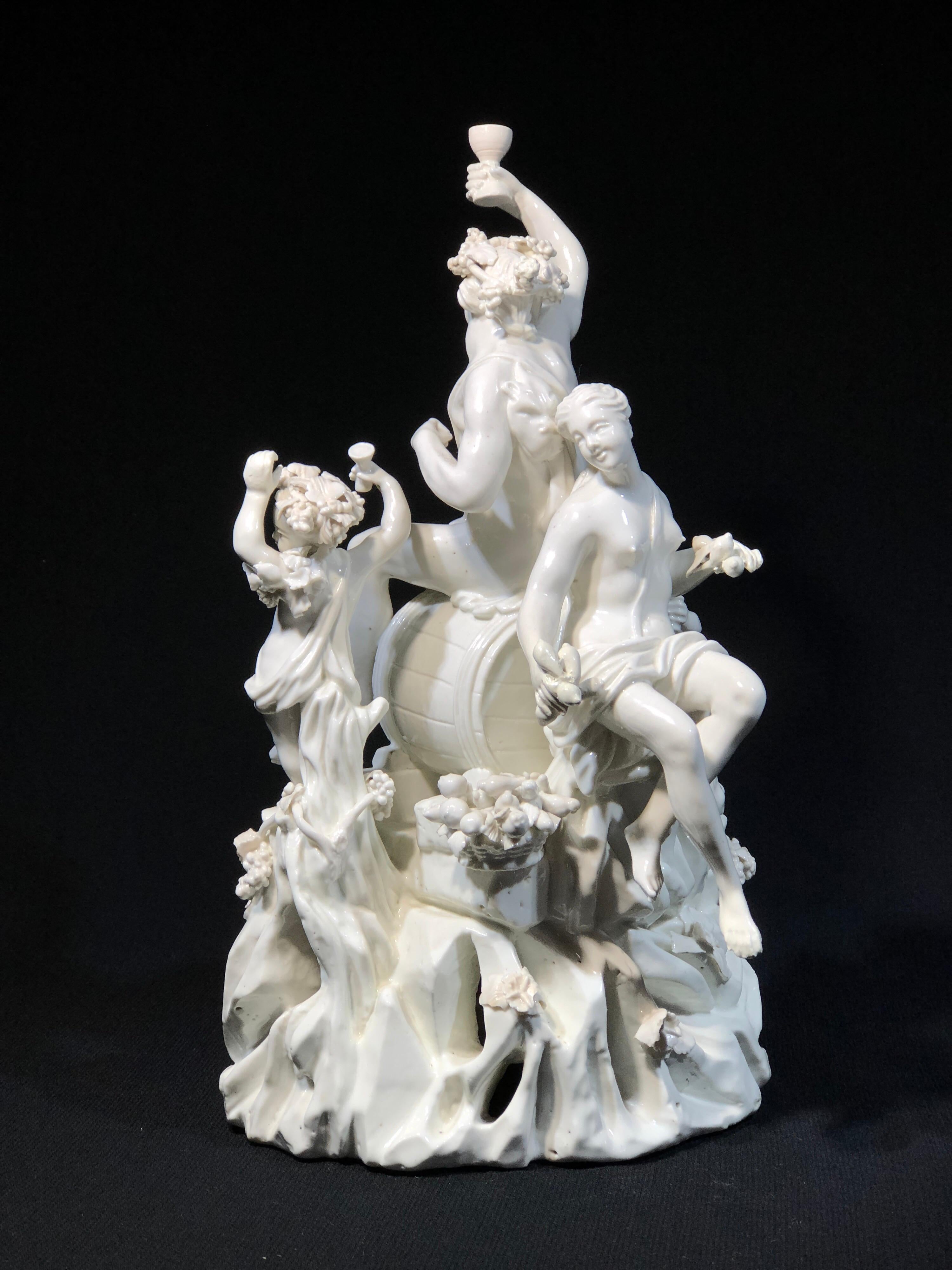 Large French porcelain group, depicting Bacchus and his revelling band, each with grapevines in their hair and a drink in hand, one re-filling from the barrel Bacchus is seated on, modelled in the round on a rocky mountain, overgrown with fruiting