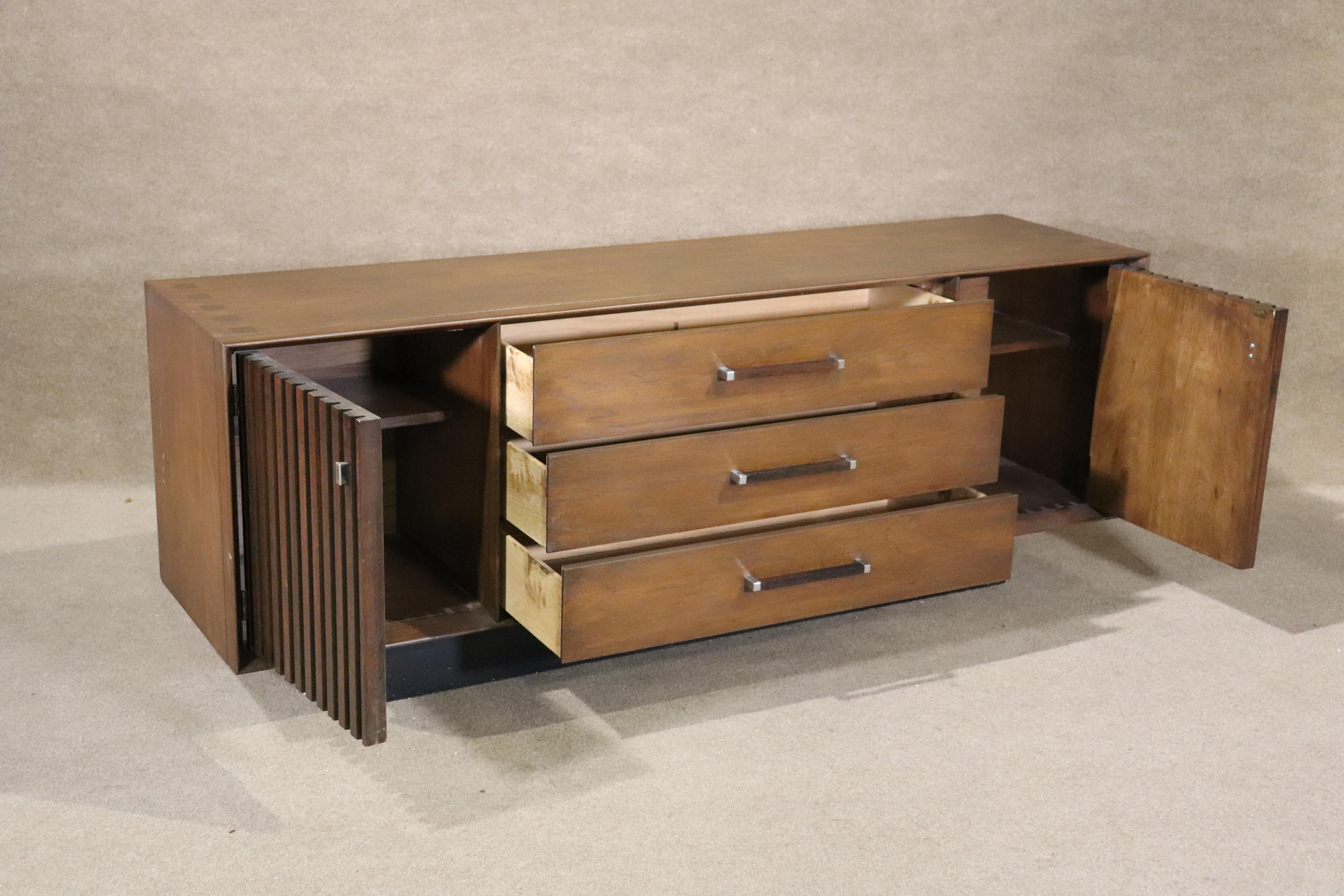 This long mid-century modern unit has dresser drawers and cabinets storage. Walnut grain wood with accenting rosewood slats and top inlay.
Please confirm location NY or NJ
