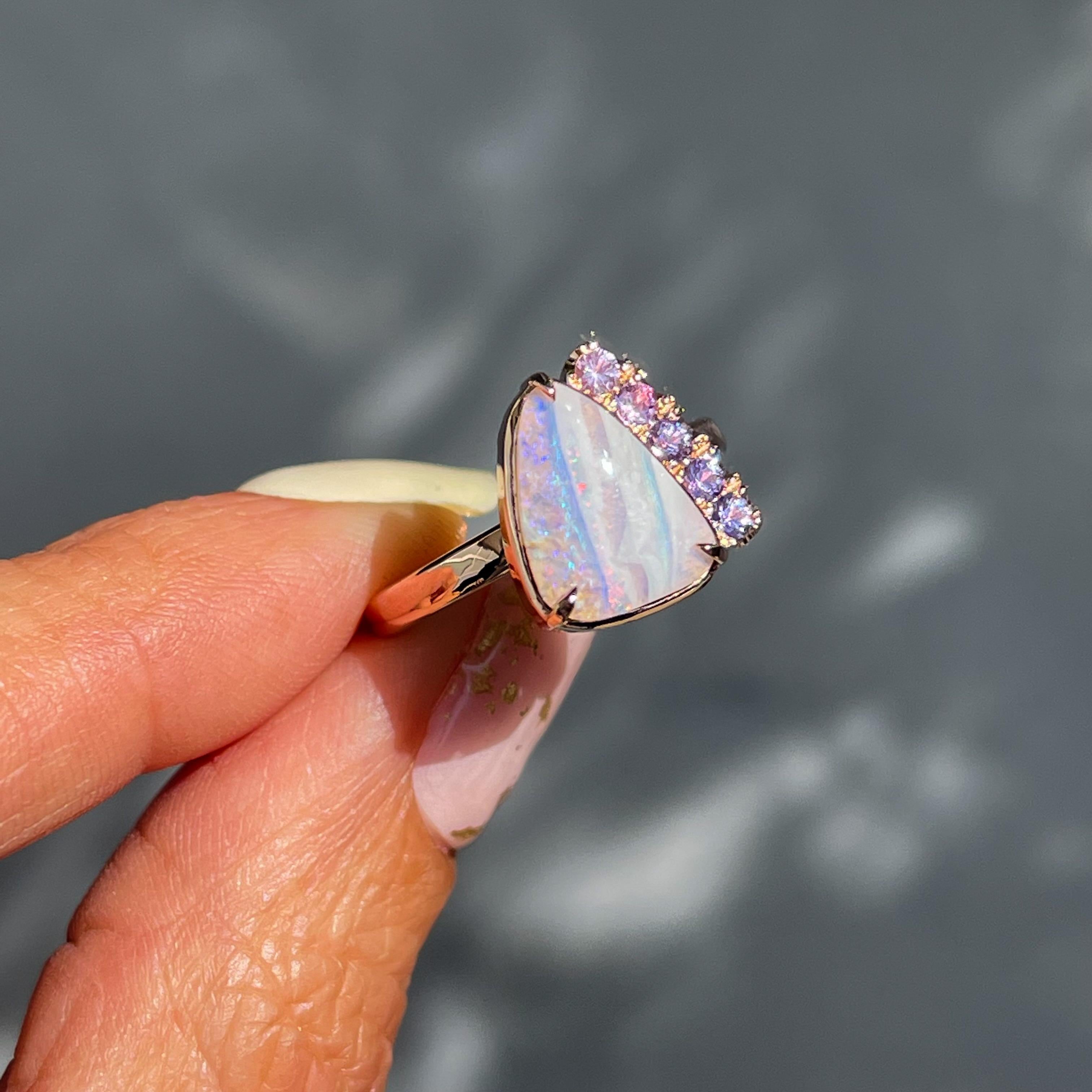 This Australian Opal Engagement Ring emanates the essence of love. Pink and purple sapphires embrace a natural opal, resulting in a stunning sapphire and opal ring. Diffused pastels streak across the stone, flashes of turquoise pulsing against the