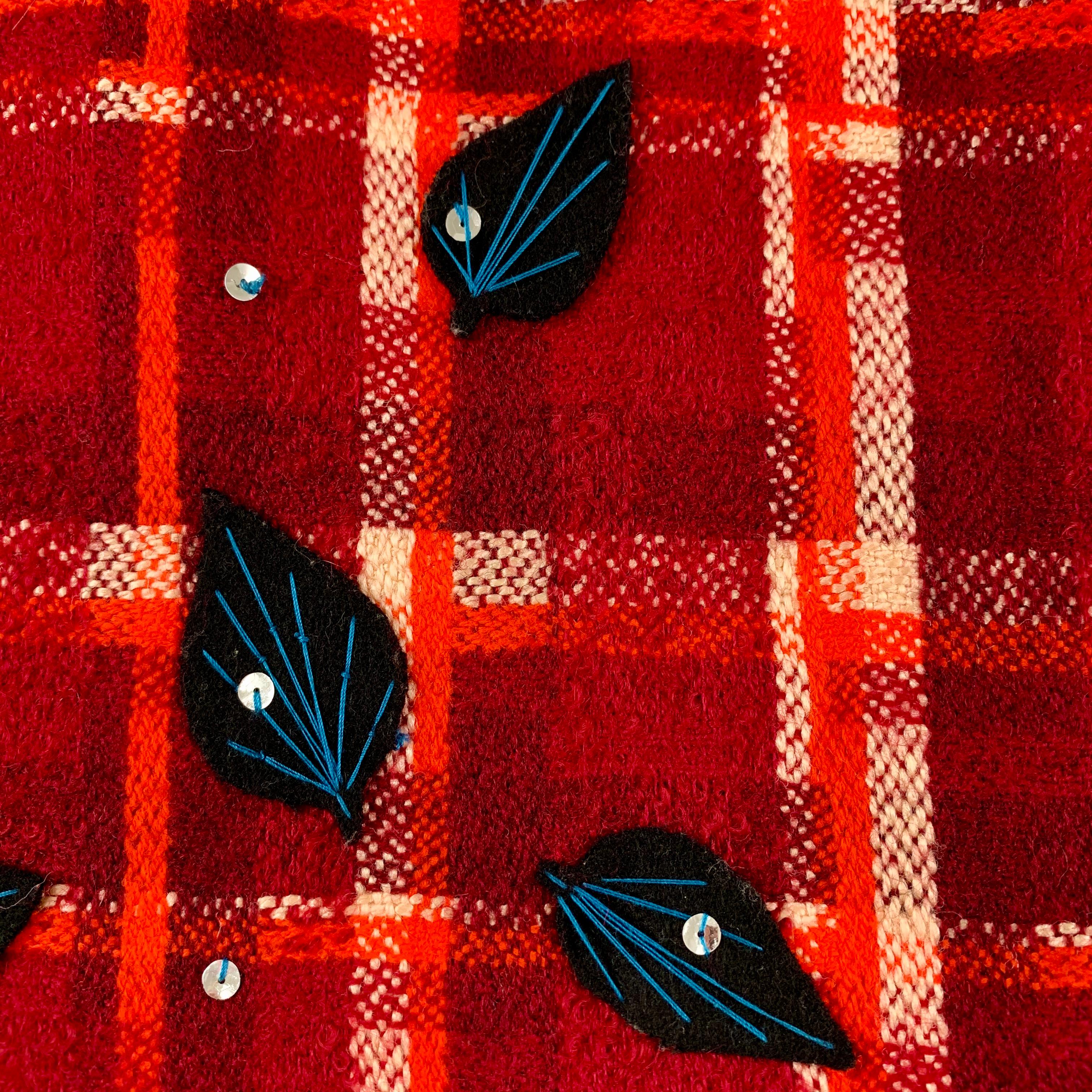 De Tracy Feith, une mini-jupe vintage bohème chic des années 1980, en laine écossaise avec des appliques cousues à la main de paillettes et de feuilles avec des broderies surpiquées.

La jupe à carreaux rouge, orange et blanc est ornée de