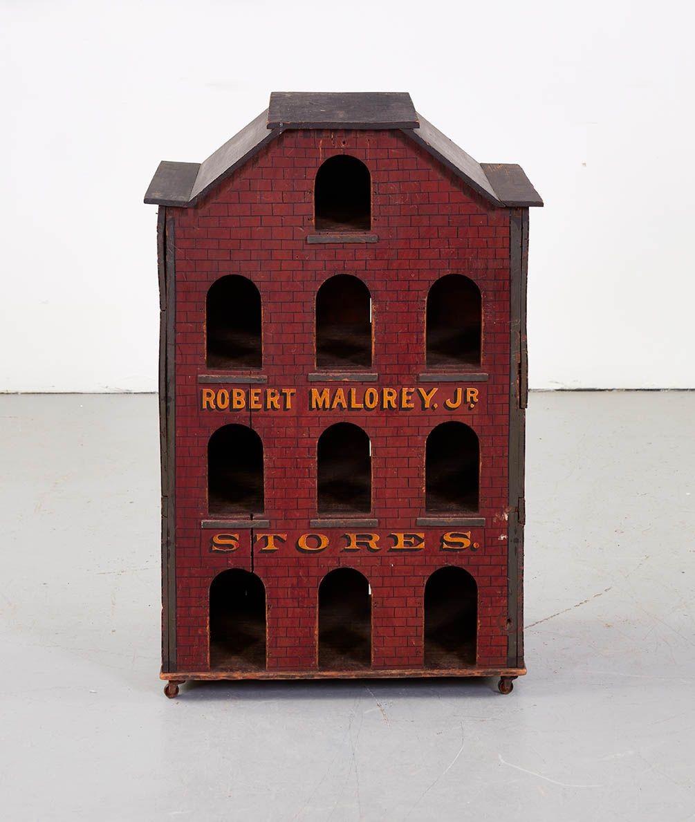 An advertising device or tradesign in the form of a brick storehouse, with ten arched windows or pigeonholes to display merchandise, constructed as a roofed box mounted on wheels, for use either on a shop floor or on a countertop. American, circa