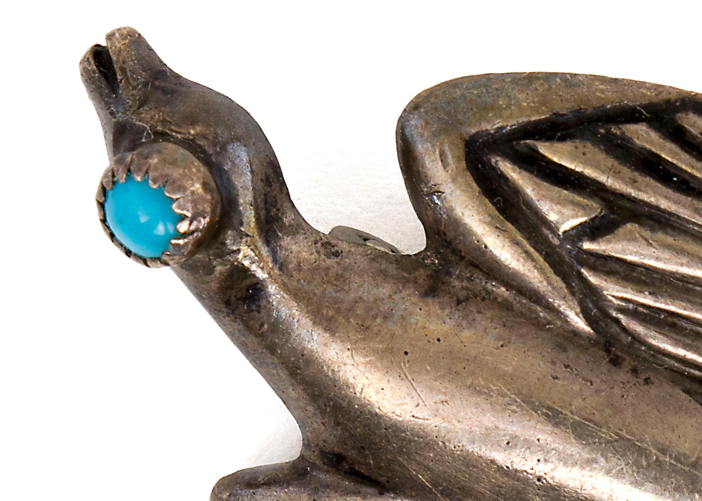 1950s silver pin in the shape of a peyote bird with a turquoise eye and detailed wings, measuring 2 x 1 inches. The pin features a small needle on the back for attachment. 

