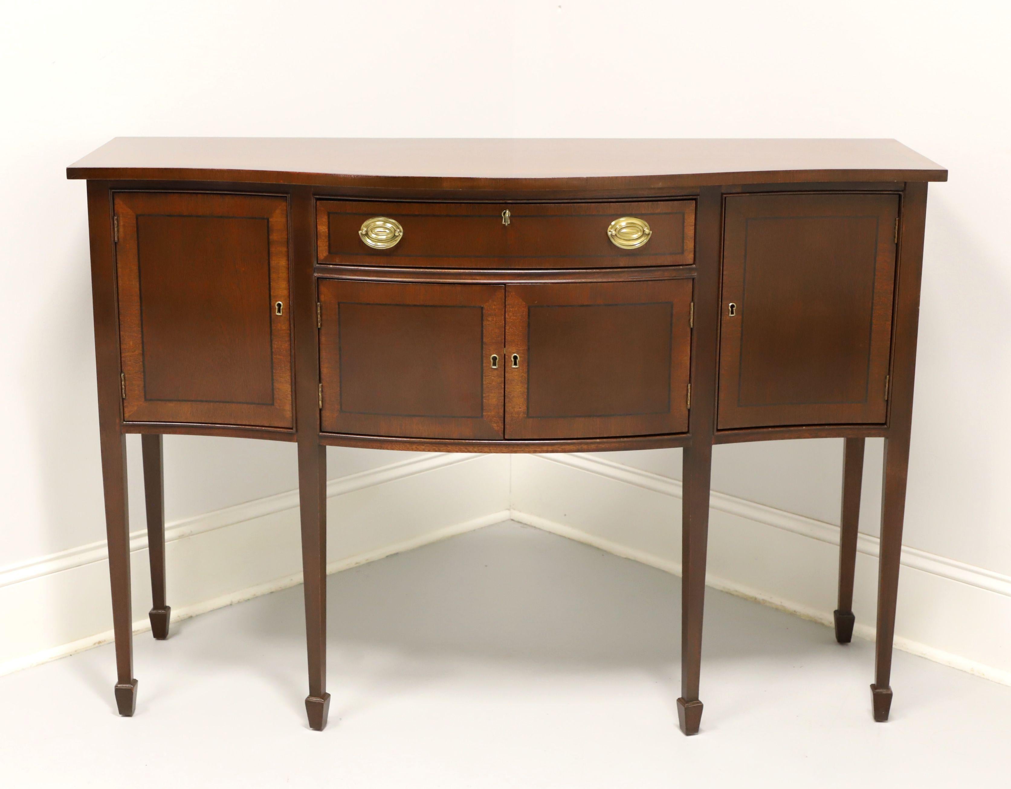 A Hepplewhite style sideboard by Tradition House, of Hanover, Pennsylvania, USA. Mahogany with brass hardware, banded top, bowfront, banded door & drawer fronts, straight tapered legs and spade feet. Features a center lockable drawer that has felt
