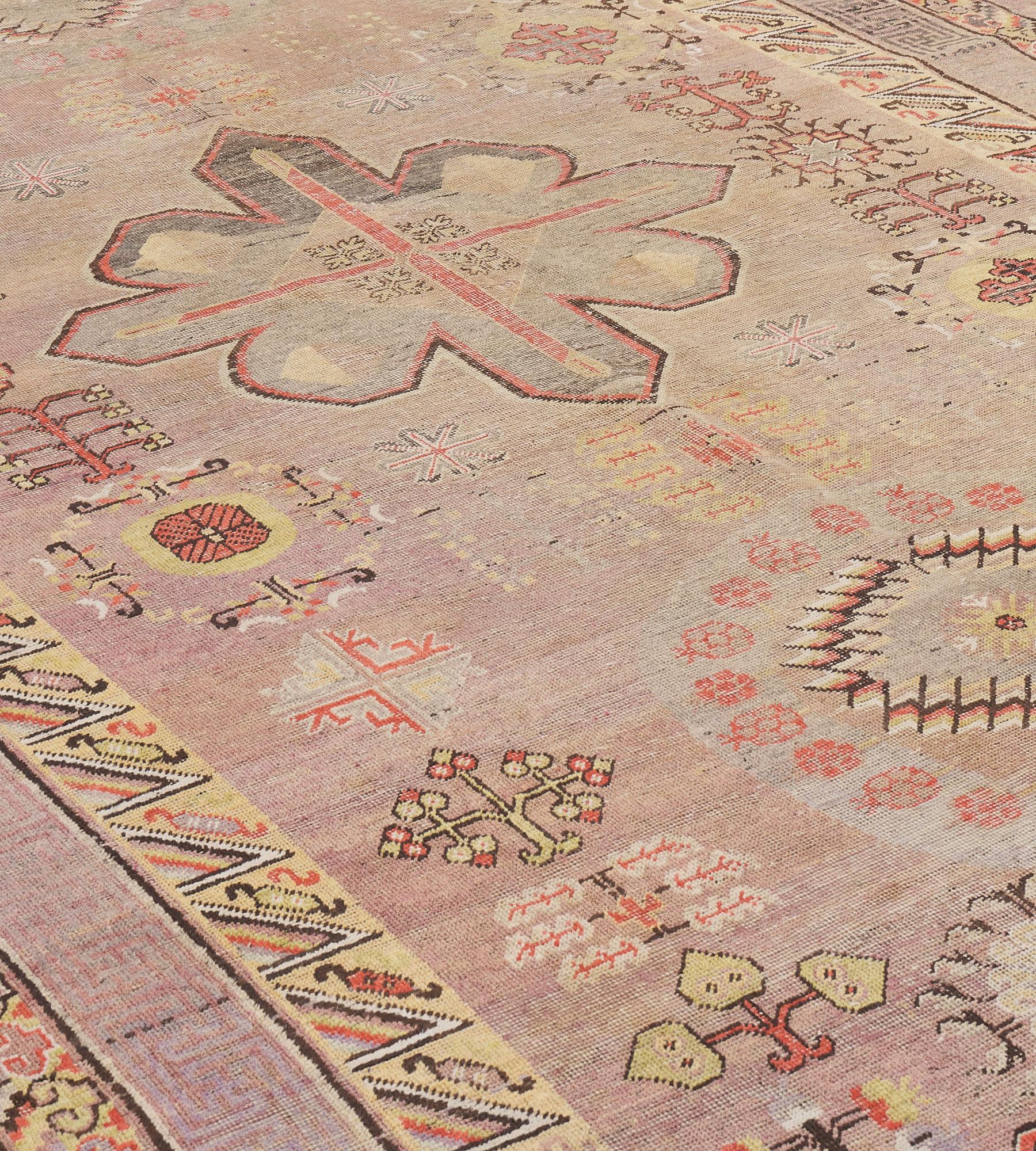 Dieser antike Khotan-Teppich hat ein schattiertes, hellpflaumenfarbenes Feld mit einem zentralen, schattierten, kohlschwarzen Medaillon mit kreisförmigen Rondellen oberhalb und unterhalb jedes Rondells mit einem Band aus Granatäpfeln um eine