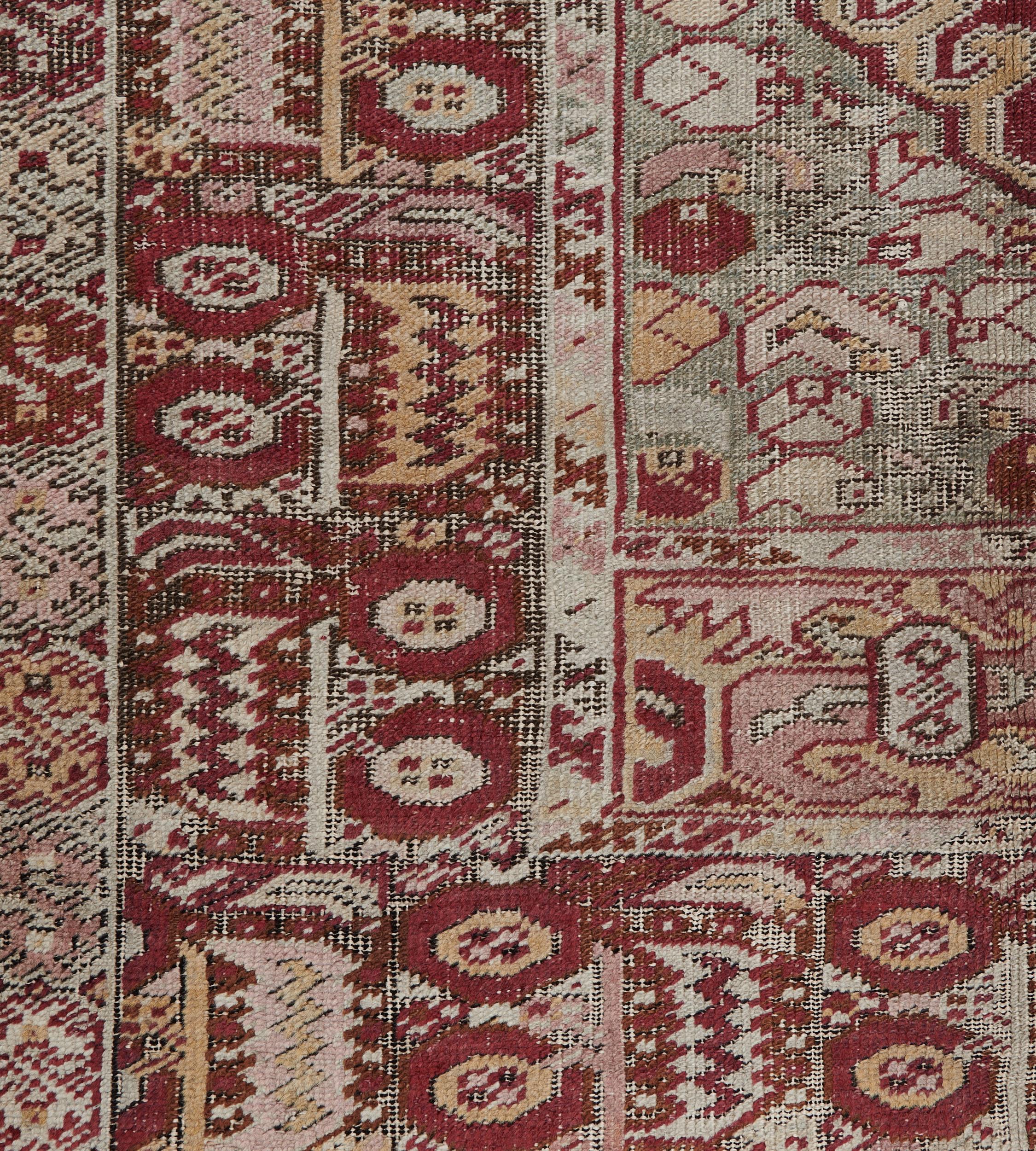 This traditional hand-woven Turkish Ghordes rug has a ruby field of flowering vases and cypress trees, in a chartreuse cusped lozenge medallion, in a dense ruby-cream geometric border, inner ivory geometric stripe, outer straw geometric border.