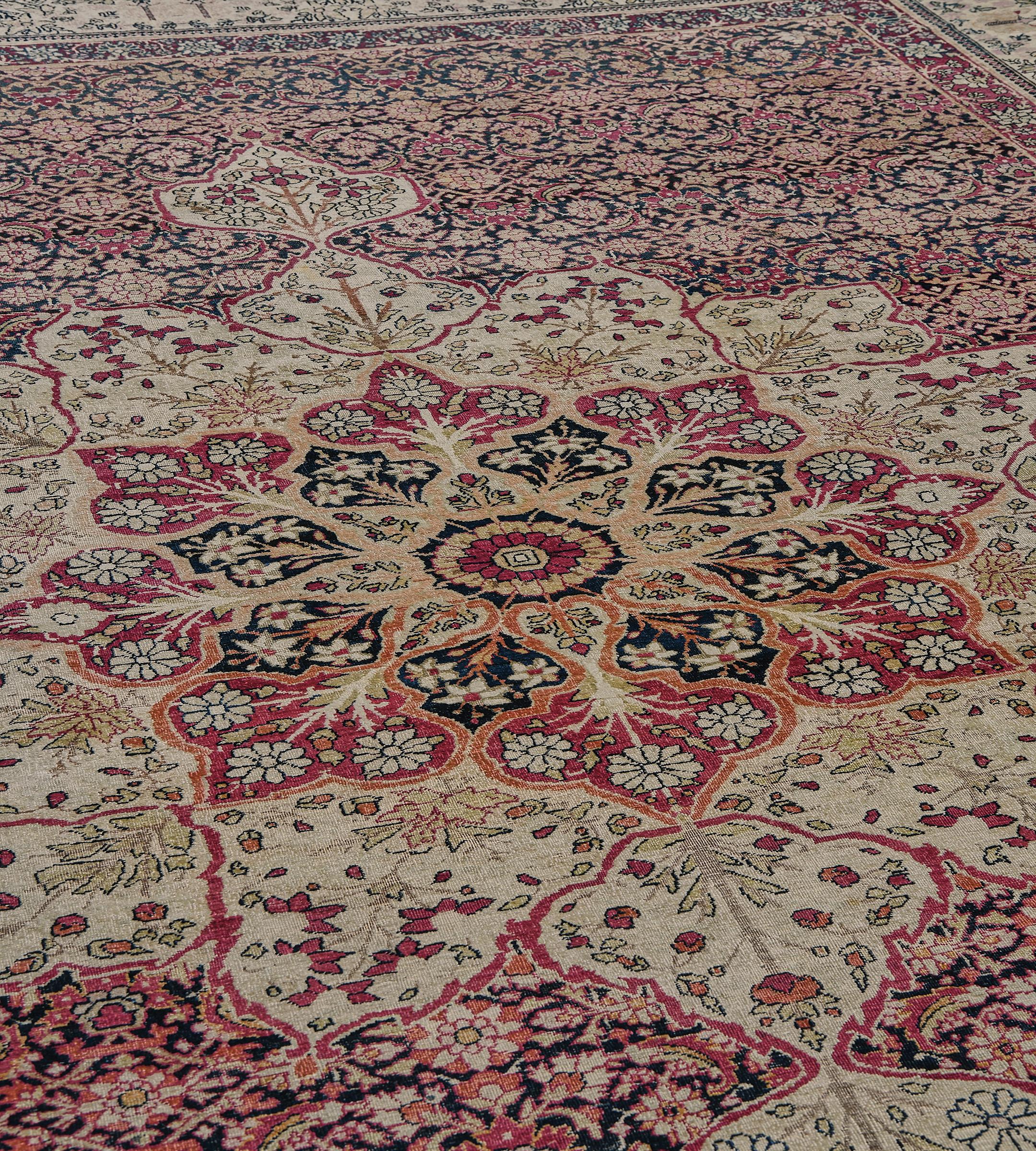 Ce tapis persan antique tissé à la main présente un champ anthracite profond avec un motif herati dense entourant un majestueux médaillon arabesque ivoire, dans une bordure ivoire équilibrée de buissons fleuris, entre des rayures polychromes ornées