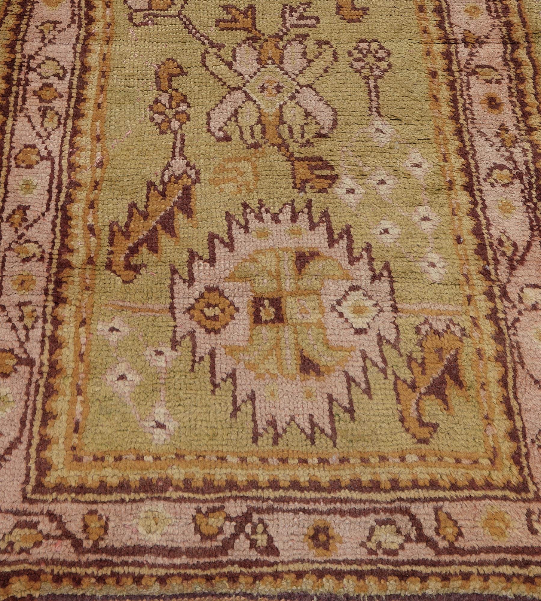 This antique, circa 1900, Anatolian Oushak runner has a light pistachio-green field with a column of dusty-pink and light pistachio-green serrated palmettes linked and surrounded by burgundy-brown and caramel-brown serrated leaf vine together with
