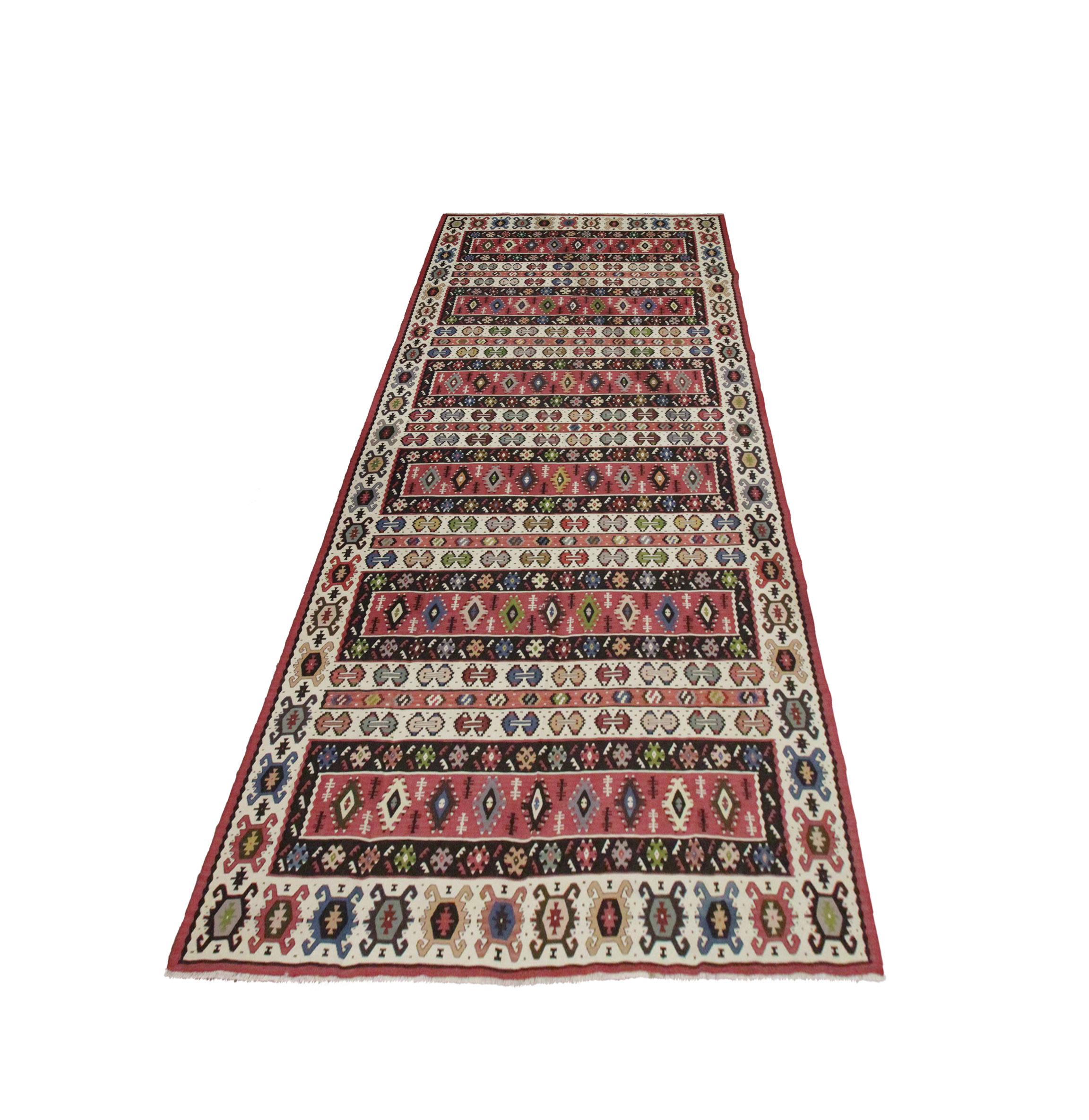 This large rug is a handwoven Serbian Kilim woven in the early 20th century. The design features a striped bold geometric pattern featuring contrasting red, beige, blue and green. The design and colours are featured together to make the perfect