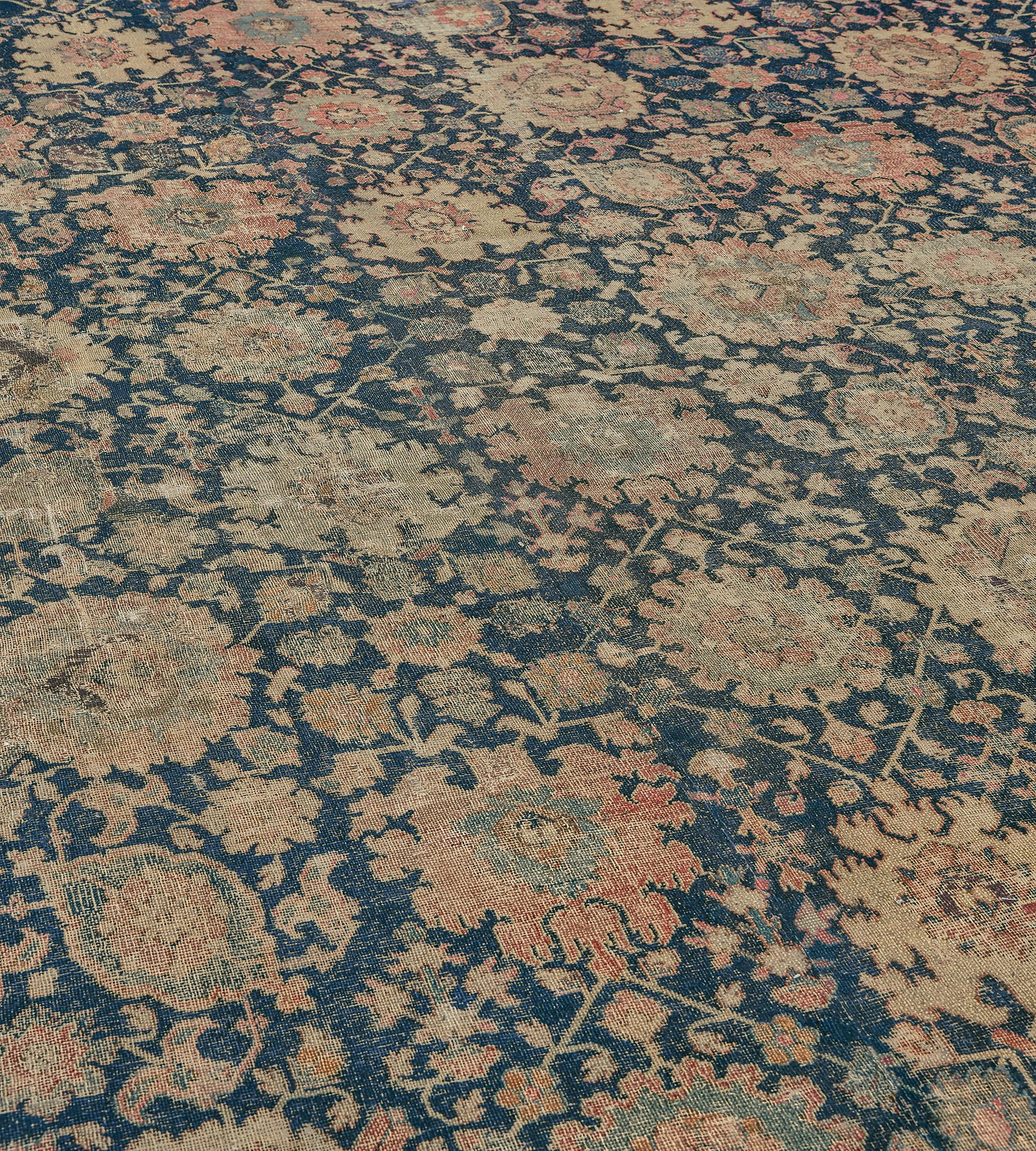 Esta alfombra tradicional persa de Isfahán tejida a mano tiene un campo añil con un diseño general de palmetas policromadas y enredaderas florales, en un elegante borde coral sombreado de arabescos serpenteantes y palmetas, entre delicadas rayas