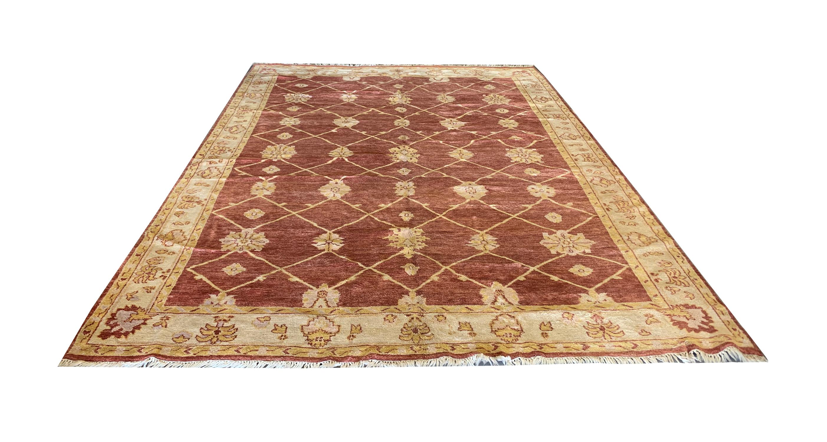 A repeating floral geometric pattern revealed in this piece is a simple yet beautiful Ziegler rug. Woven by hand in India in the 1990s, with a subtle colour palette including a brown-red background and beige-gold accents that make up the repeating