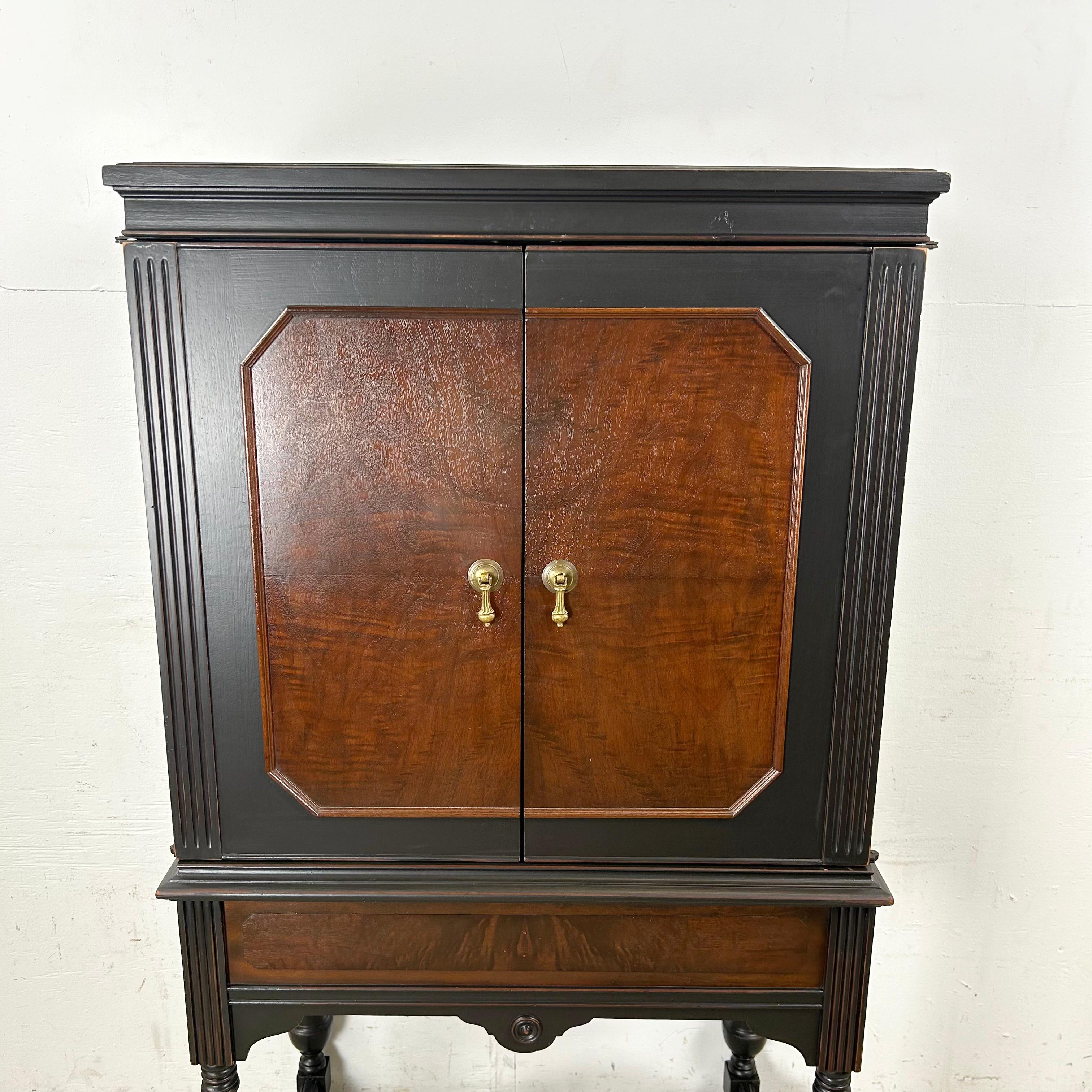 A vintage freestanding cabinet reinvented as a bar, finished in a deep relacquer with a two-tone wood contrast. Classical influences appear in the fluted columns, brass hardware, and turned legs with stretcher support, anchoring the piece in