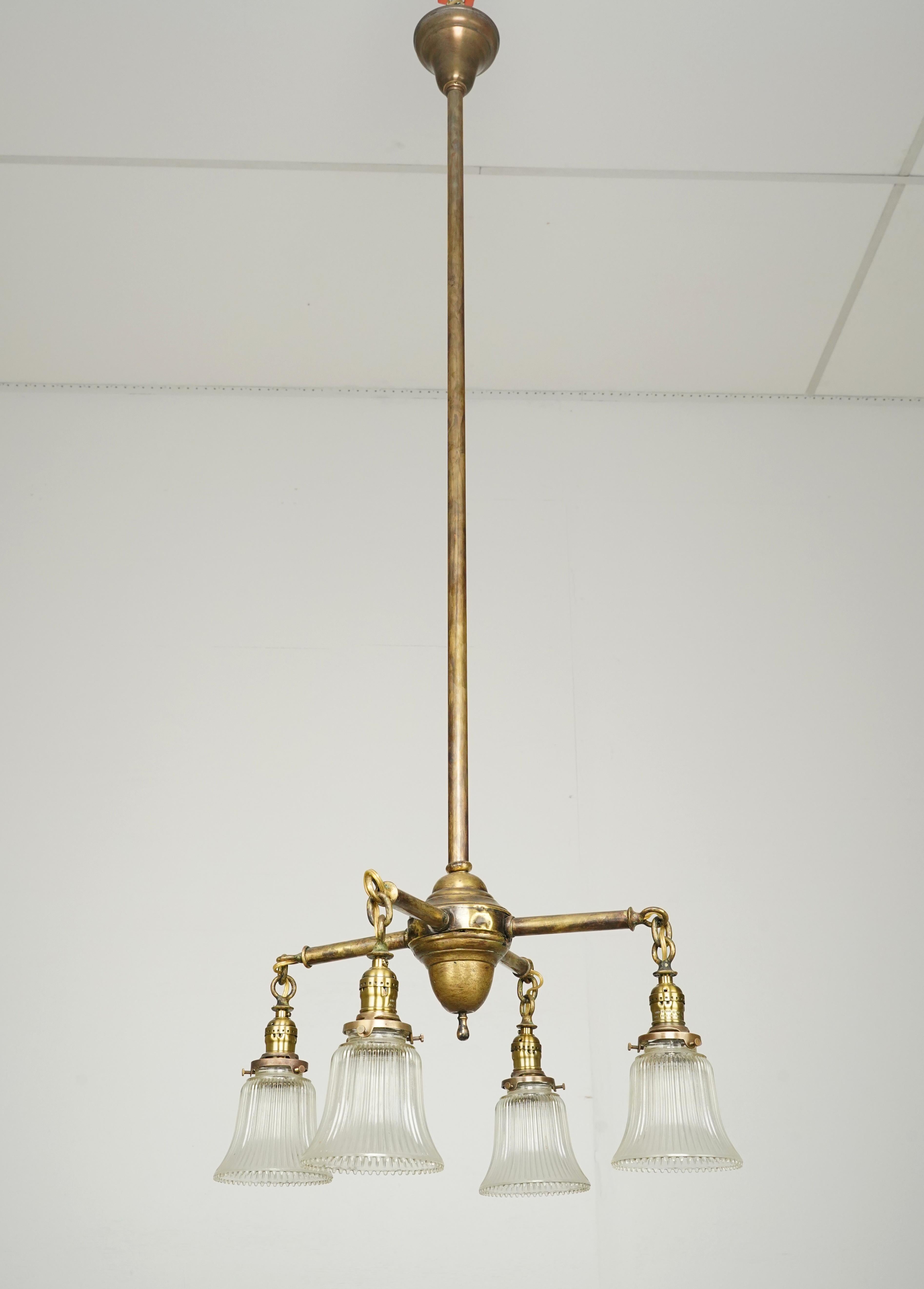 Traditional style chandelier with four arms and clear glass shades with an antique brass finish pole. This requires four standard Edison style medium base bulbs. This light is cleaned and restored and ready to ship. Good condition with surface wear